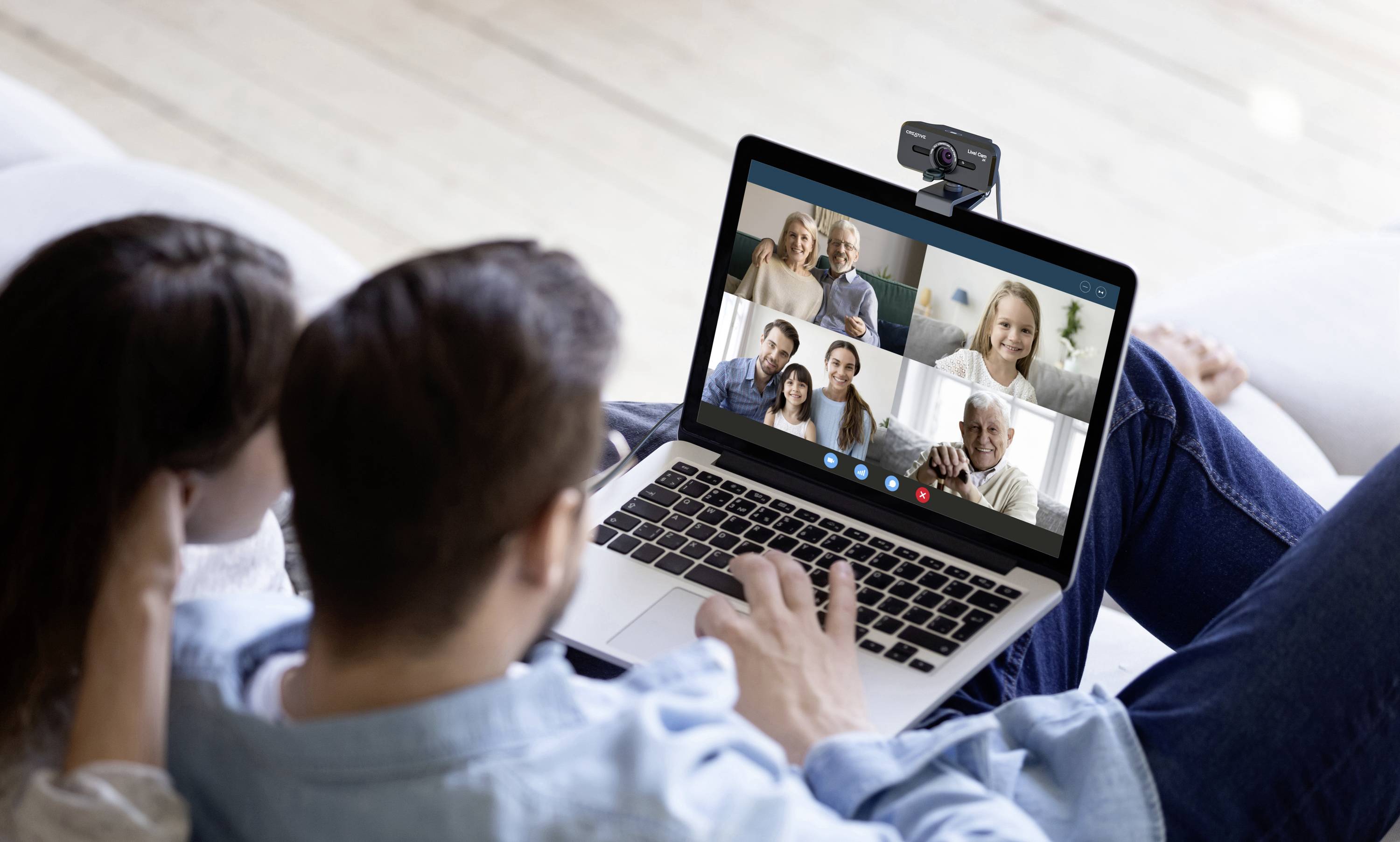 Une personne assise sur un canapé utilise un ordinateur portable pour un appel vidéo multiparticipants. La webcam est positionnée en haut de l'écran de l'ordinateur portable.