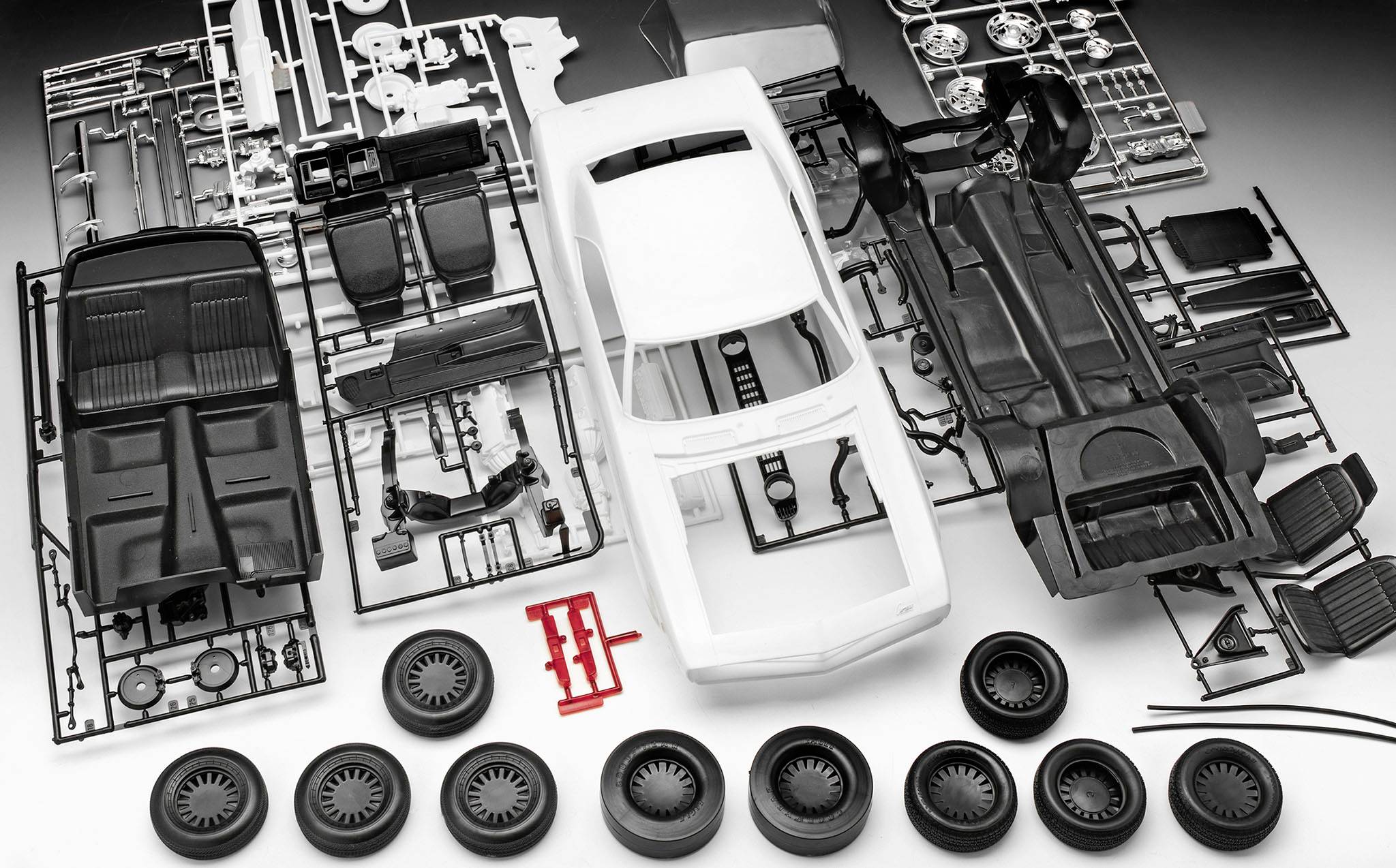 Pièces en plastique d'une voiture miniature en pièces détachées, comprenant la carrosserie, les roues et les accessoires, disposées sur une surface grise.