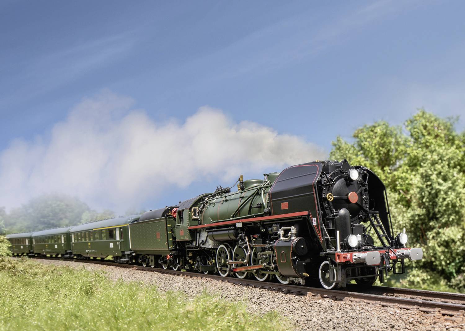 Une locomotive à vapeur historique tire plusieurs wagons verts sur une voie ferrée à travers un paysage rural sous un ciel dégagé.