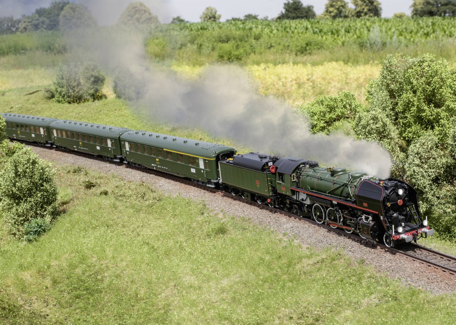 Une locomotive à vapeur fumante tire des wagons de passagers verts à travers un paysage rural avec des arbres et des champs en arrière-plan.