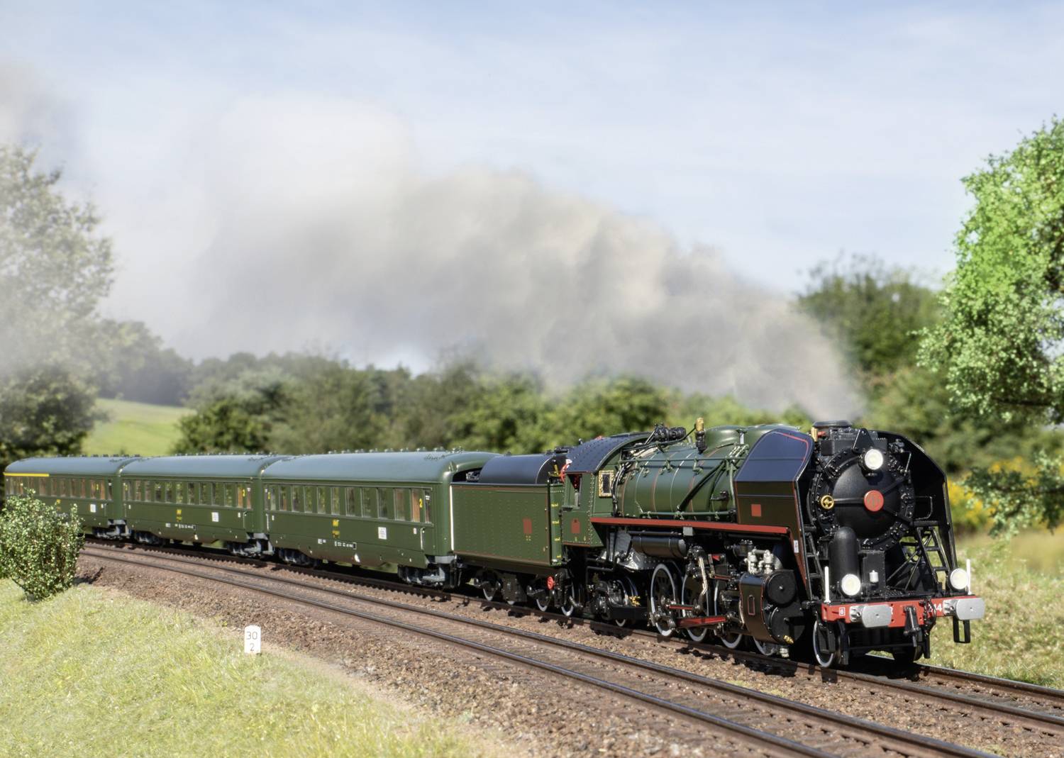 Une locomotive à vapeur tractant des wagons verts traverse un paysage verdoyant. Le ciel est légèrement nuageux.