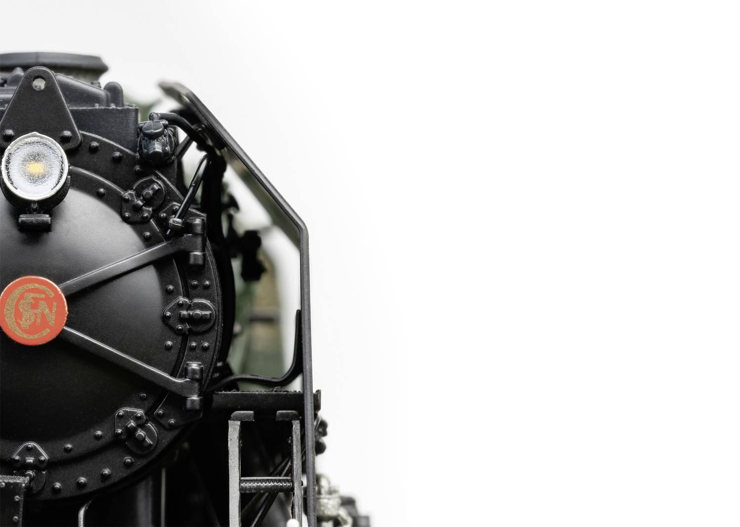 Gros plan d'une locomotive à vapeur noire sur un fond blanc. L'image montre la vue de face avec une porte ronde et un phare.