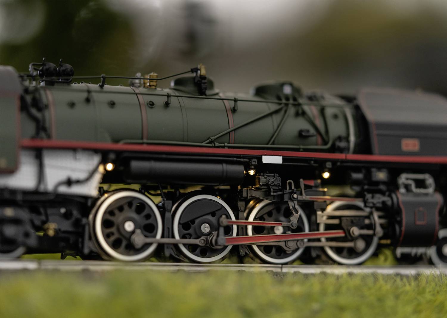 Une locomotive miniature détaillée sur des rails, entourée de verdure floue à l'avant et à l'arrière-plan. Passion pour la technique.