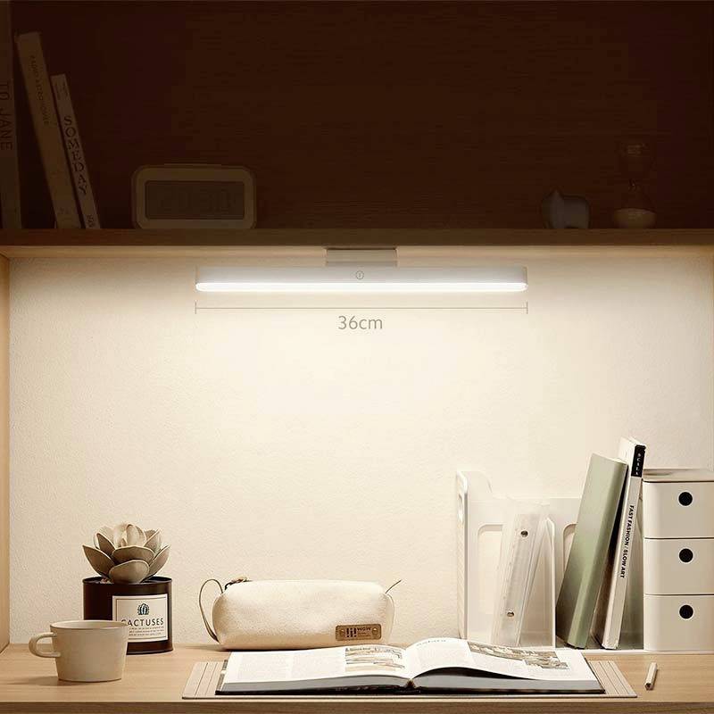 Un bureau avec une lampe LED allumée au-dessus de livres et de matériel d'écriture. L'éclairage crée une atmosphère chaleureuse et accueillante.