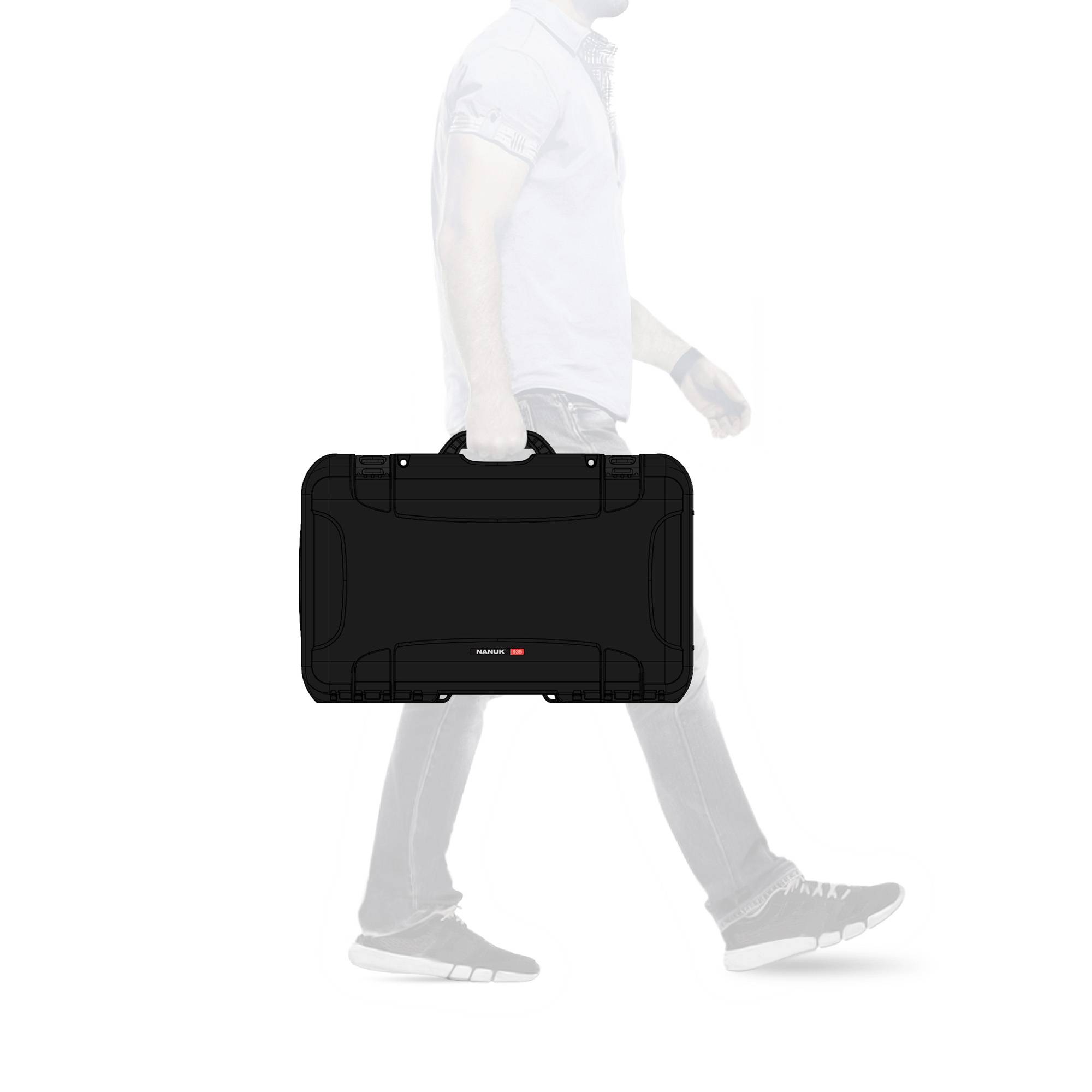 Un homme portant un jean et des chaussures blanches transporte une valise noire. L'accent est mis sur la valise, l'environnement étant estompé.