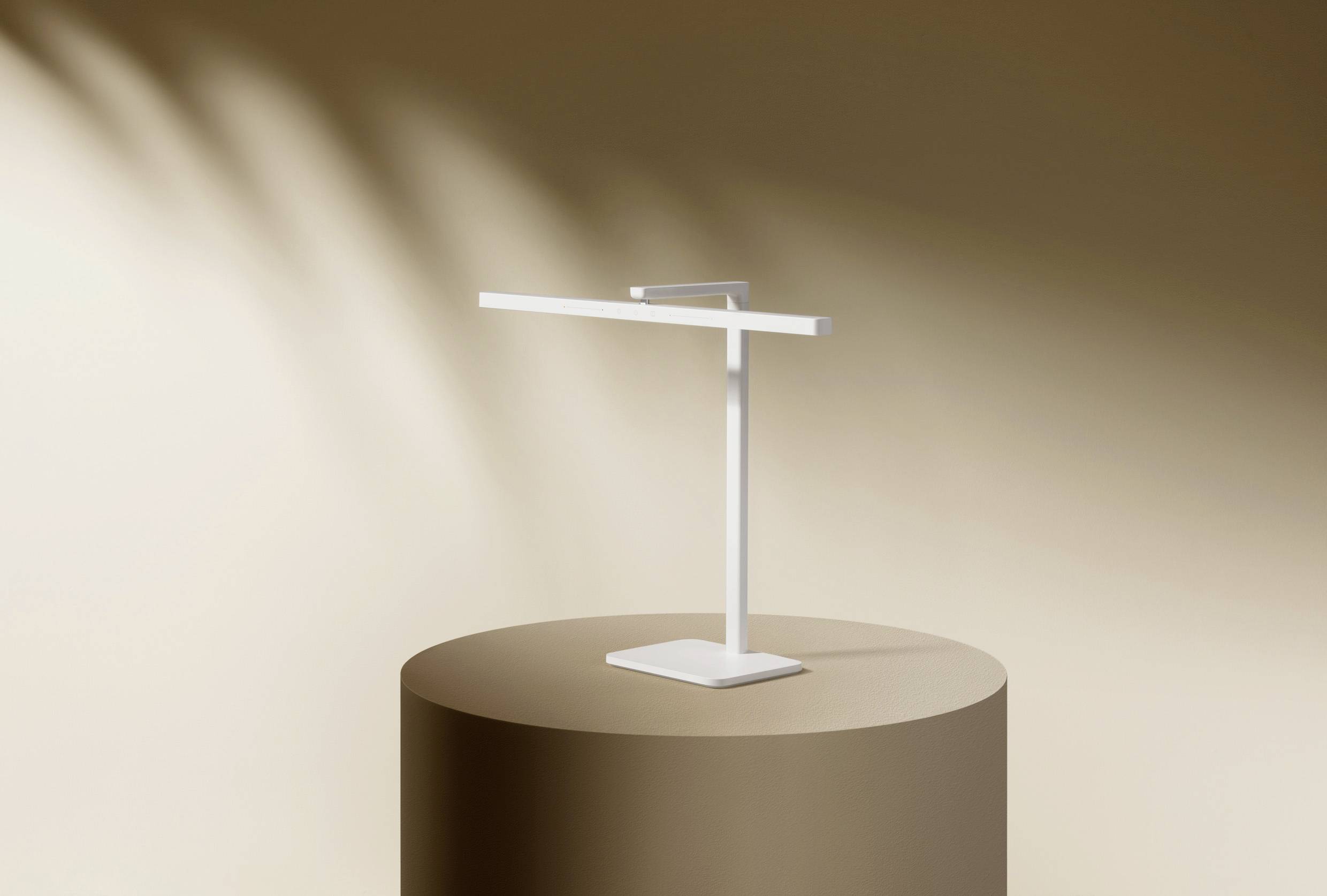 Une lampe de table minimaliste blanche est posée sur un socle cylindrique brun devant un fond beige.