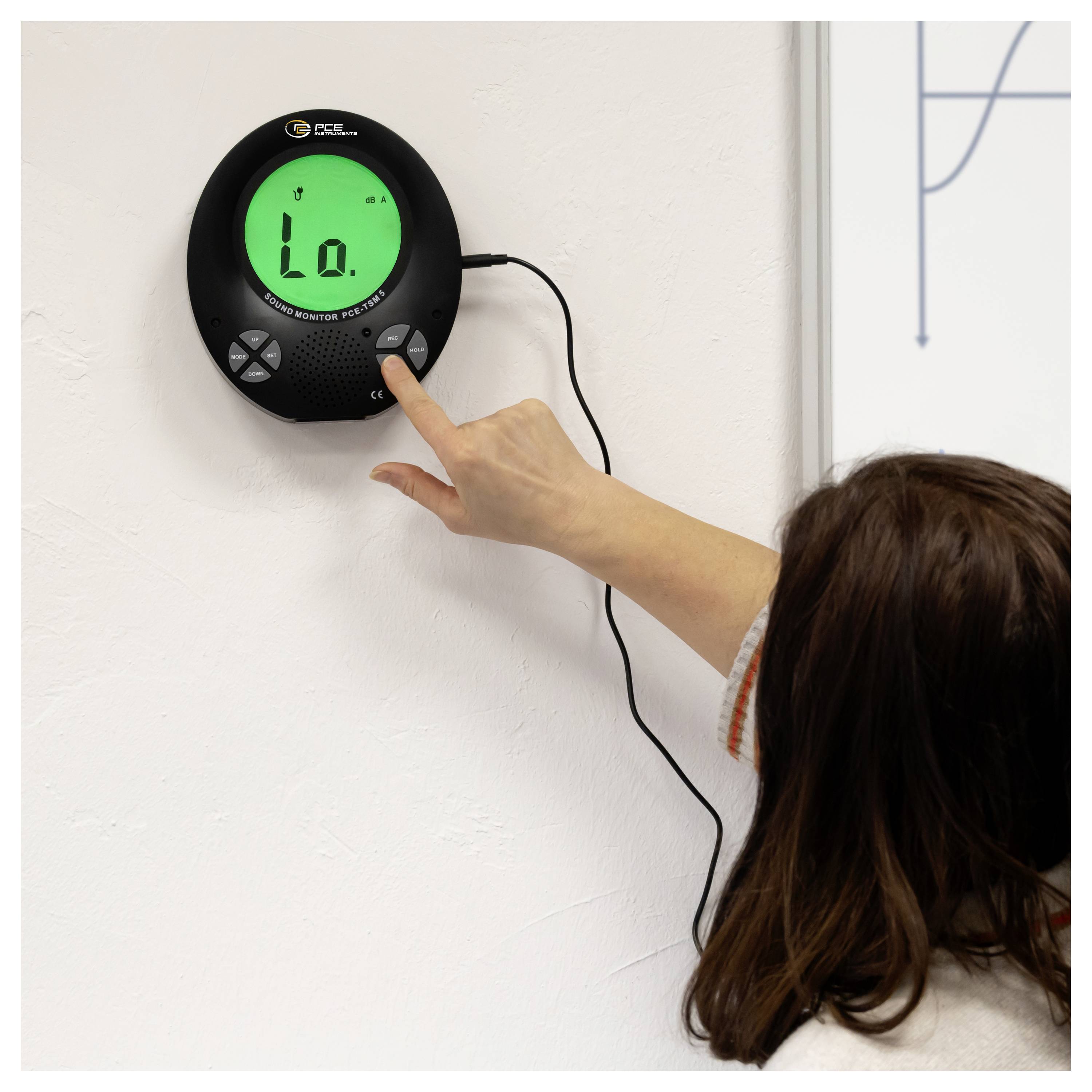 Une personne appuie sur un moniteur numérique fixé au mur affichant « Lo. », probablement pour vérifier ou ajuster une lecture de capteur intérieur.