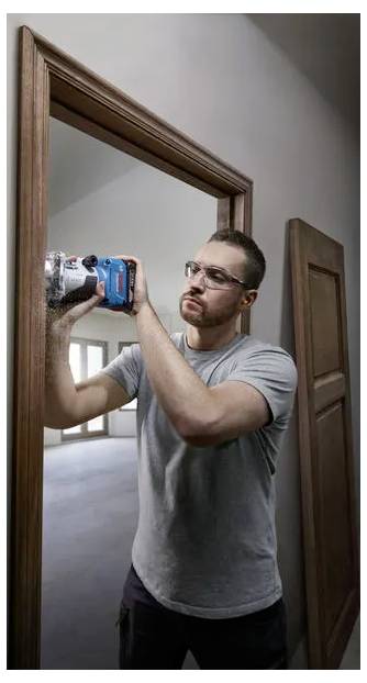 Un homme utilisant une perceuse sans fil pour installer ou réparer un cadre de porte en bois à l'intérieur.