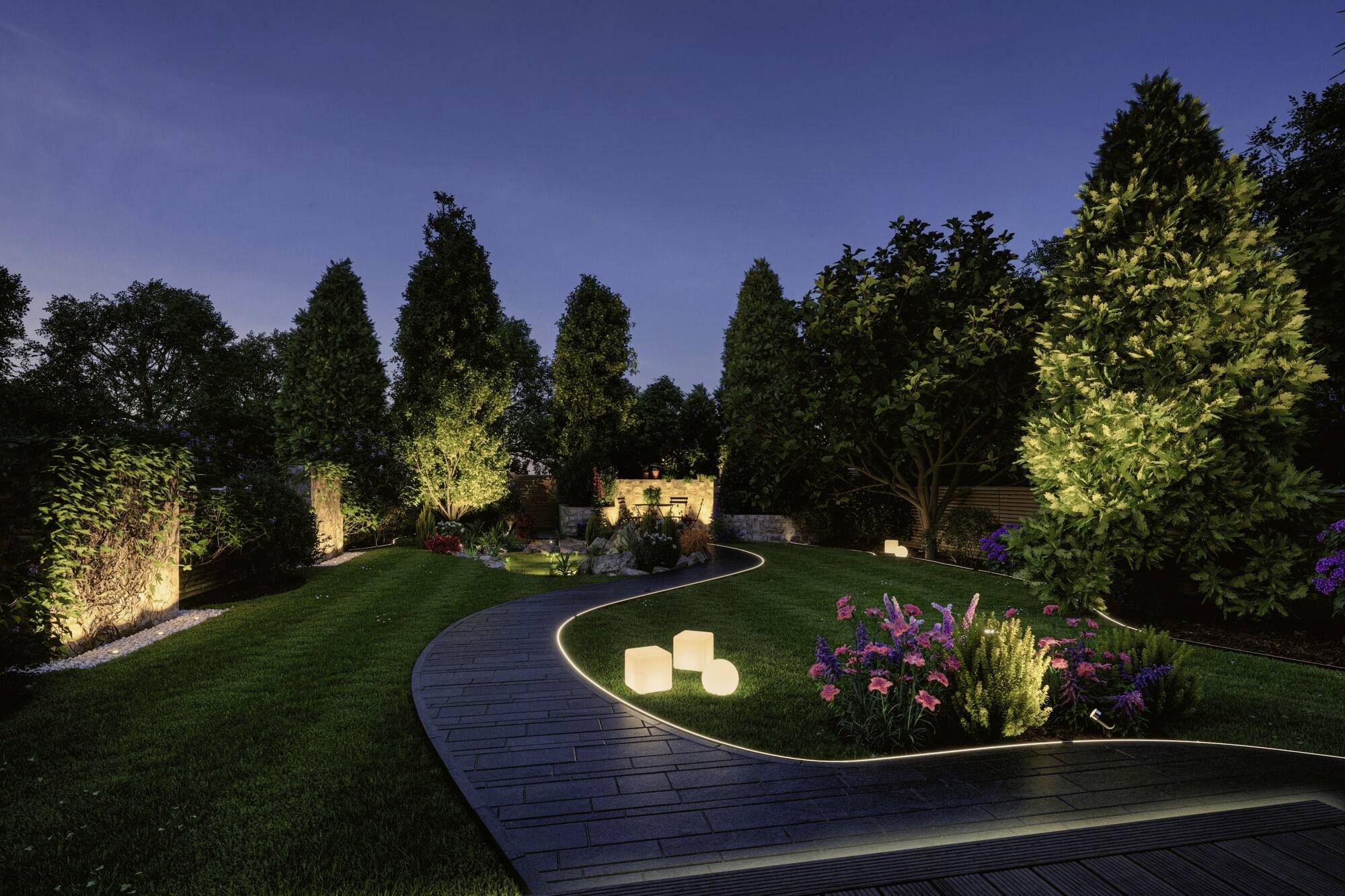 Un jardin soigné la nuit, illuminé par des cubes lumineux et des lampes de sentier, entouré d'arbres élevés et éclairés.