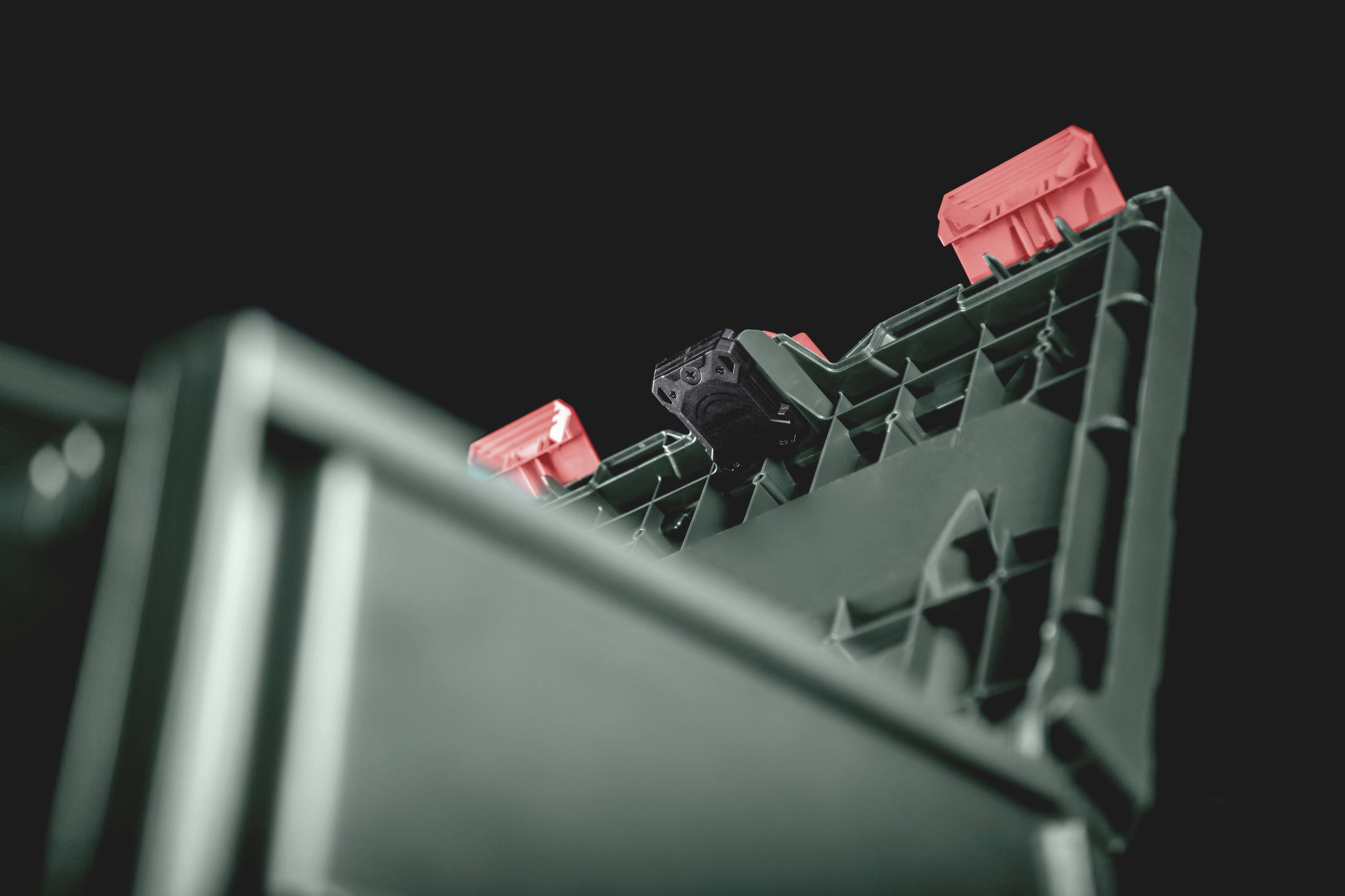 Gros plan d'un récipient en plastique noir avec des bouchons rouges, sur un fond sombre. La structure du récipient est bien visible.