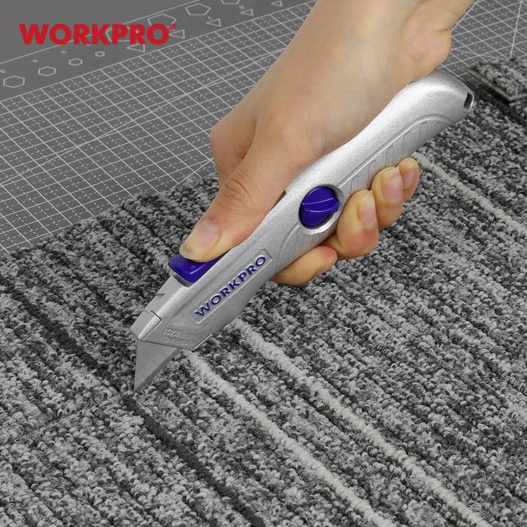 Une main coupe un tapis gris structuré avec un cutter gris, posé sur un tapis de coupe.