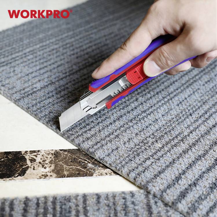 Une main tient un couteau à tapis et coupe un tapis gris sur un fond clair.