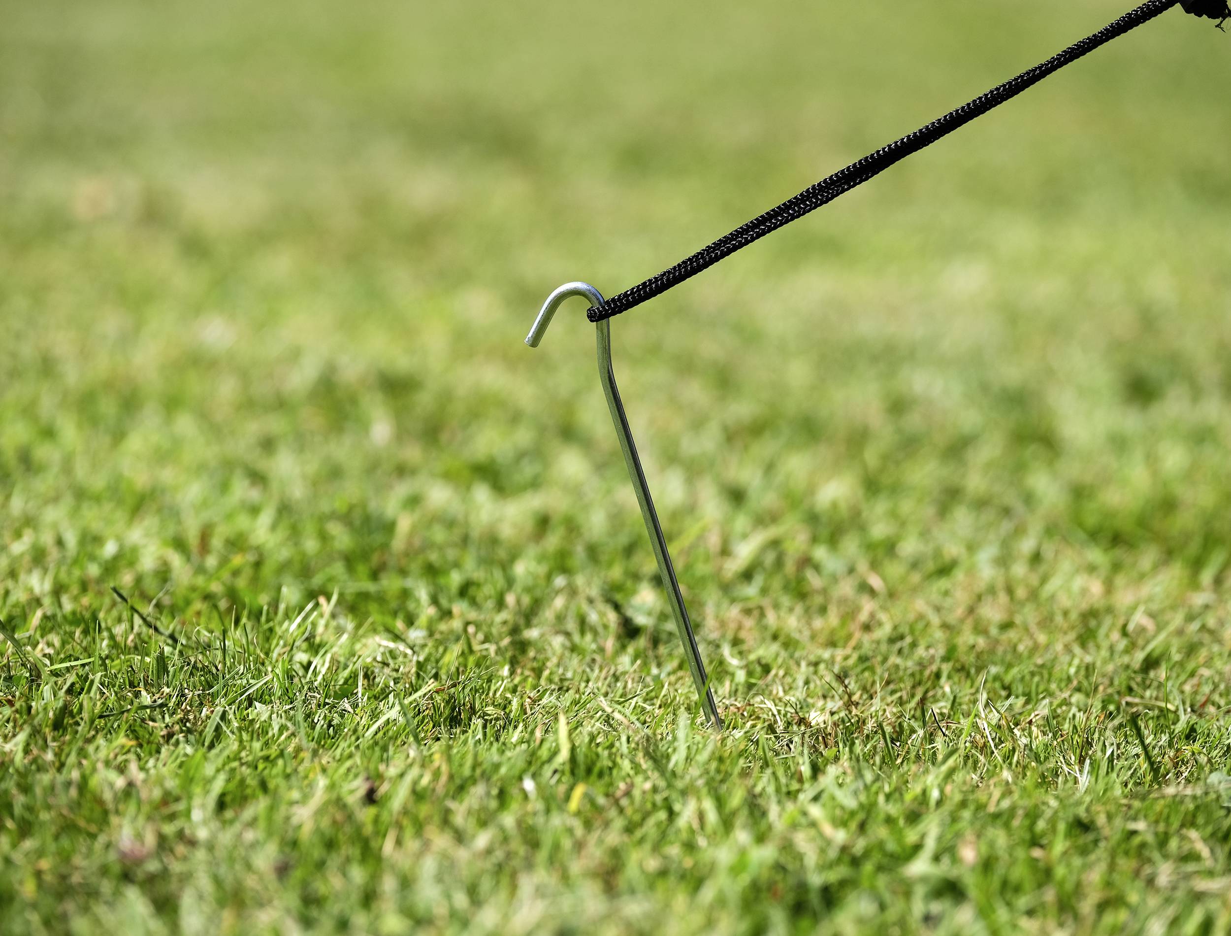 Un piquet de tente en métal qui maintient une corde tendue sur un pré vert.