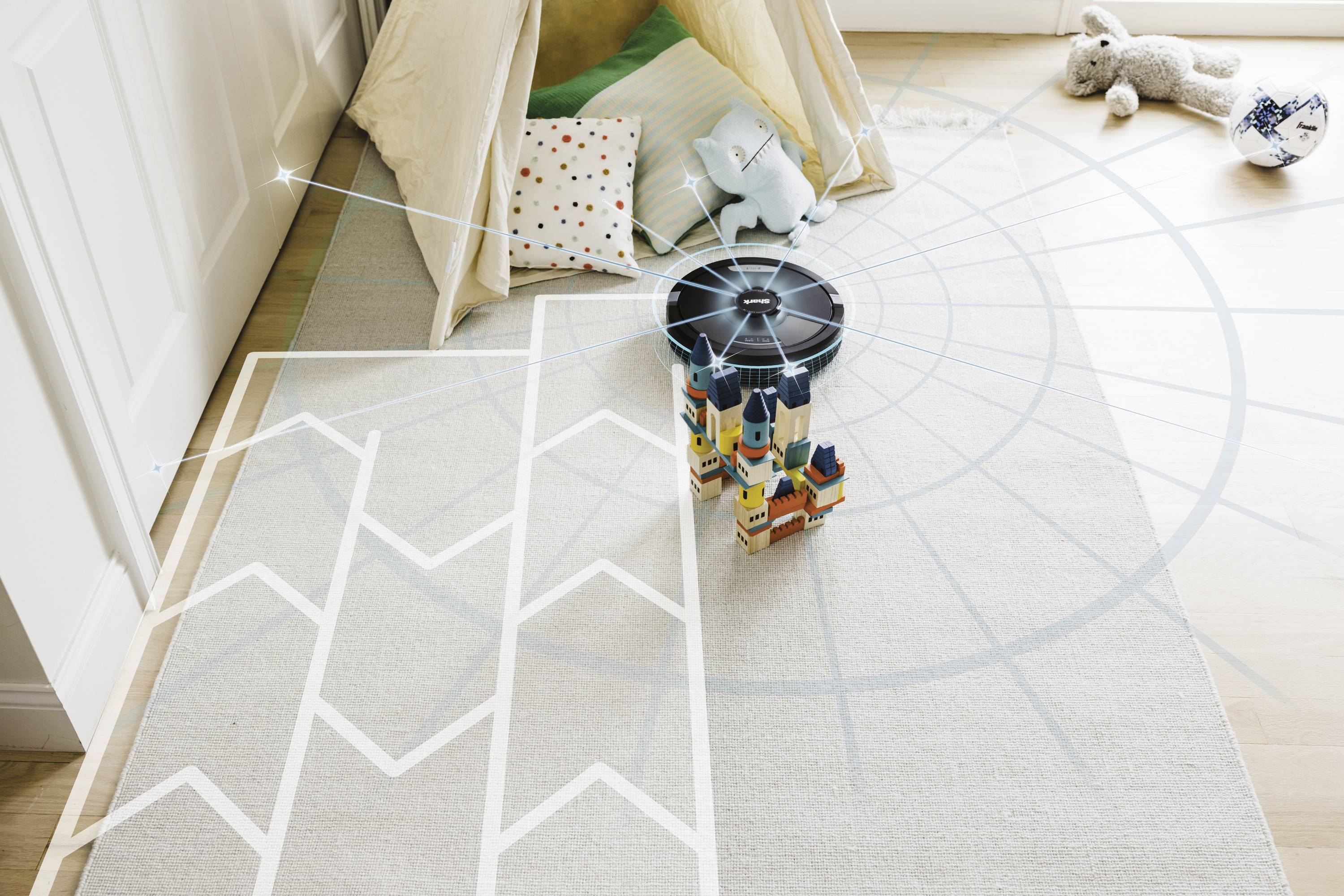 Une chambre d'enfant avec un sol en bois, une tente garnie de coussins, et des jouets éparpillés sur le sol, dont une peluche et des cubes de construction.