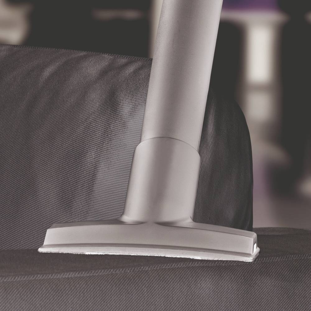 Un tuyau d'aspirateur aspire une housse en tissu gris foncé. À l'arrière-plan, des couleurs floues sont visibles.