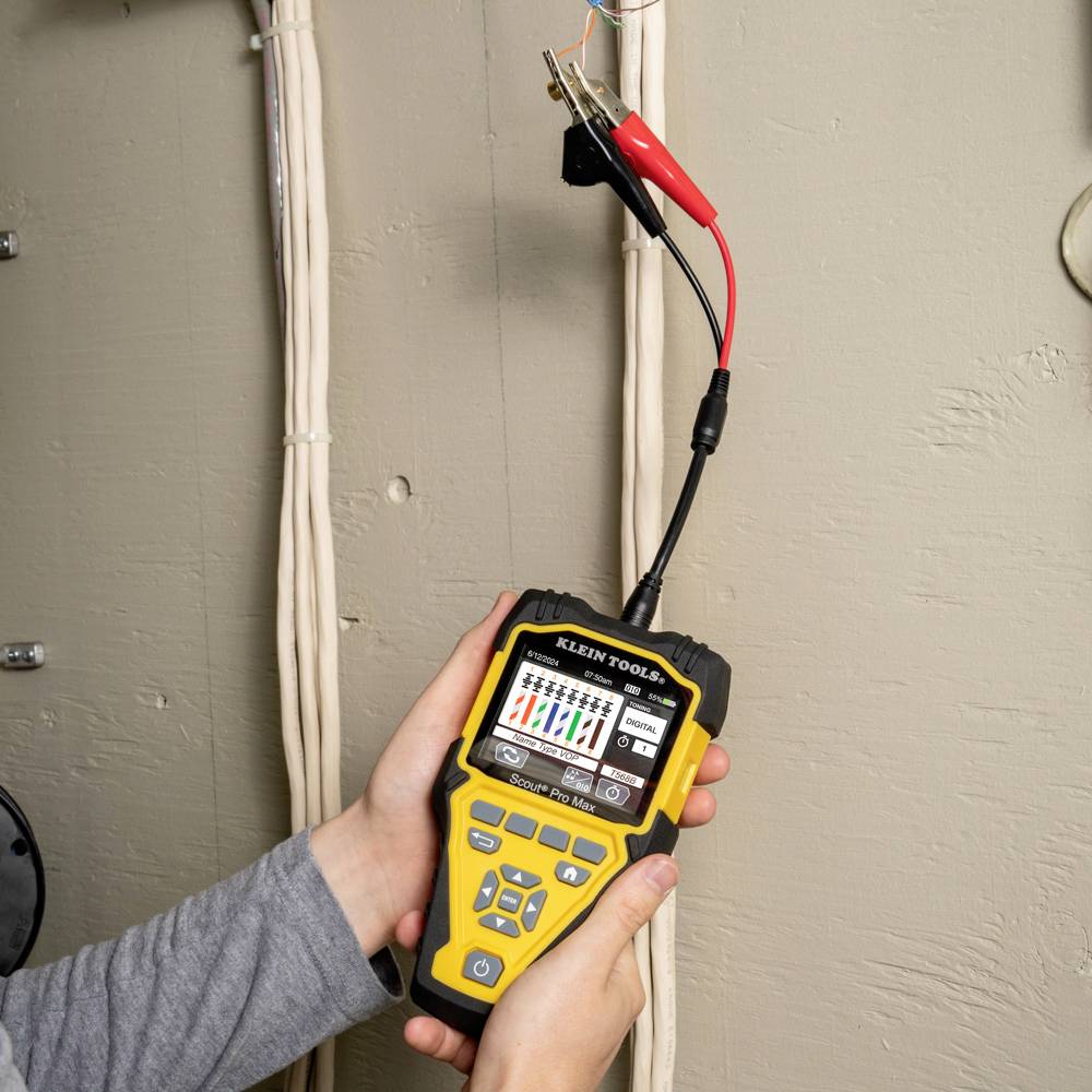 Une personne teste des lignes électriques avec un multimètre jaune, fixé aux câbles à l'aide de pinces rouges et noires.