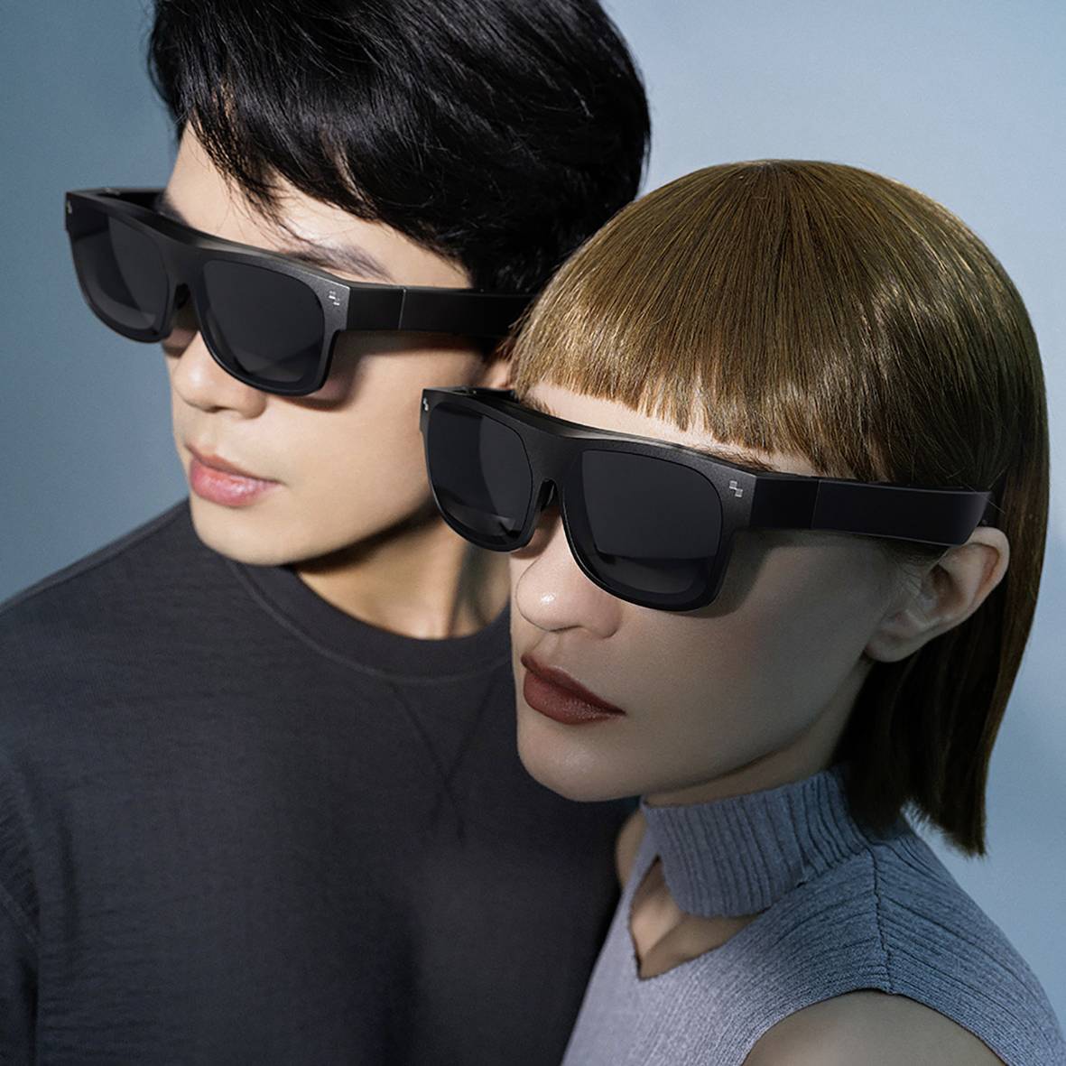 Deux personnes portent des lunettes de réalité virtuelle modernes et noires. Elles regardent dans la même direction. L'arrière-plan est neutre.