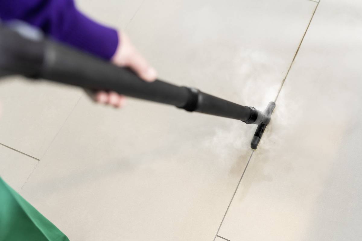 Une personne utilise un nettoyeur vapeur sur un sol carrelé, en se concentrant sur les joints de carrelage.
