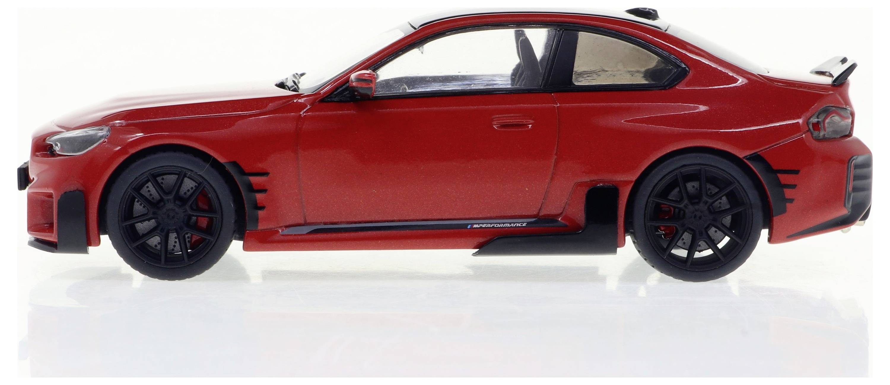 Une voiture miniature rouge de profil avec des jantes noires et un design sportif sur un fond blanc.