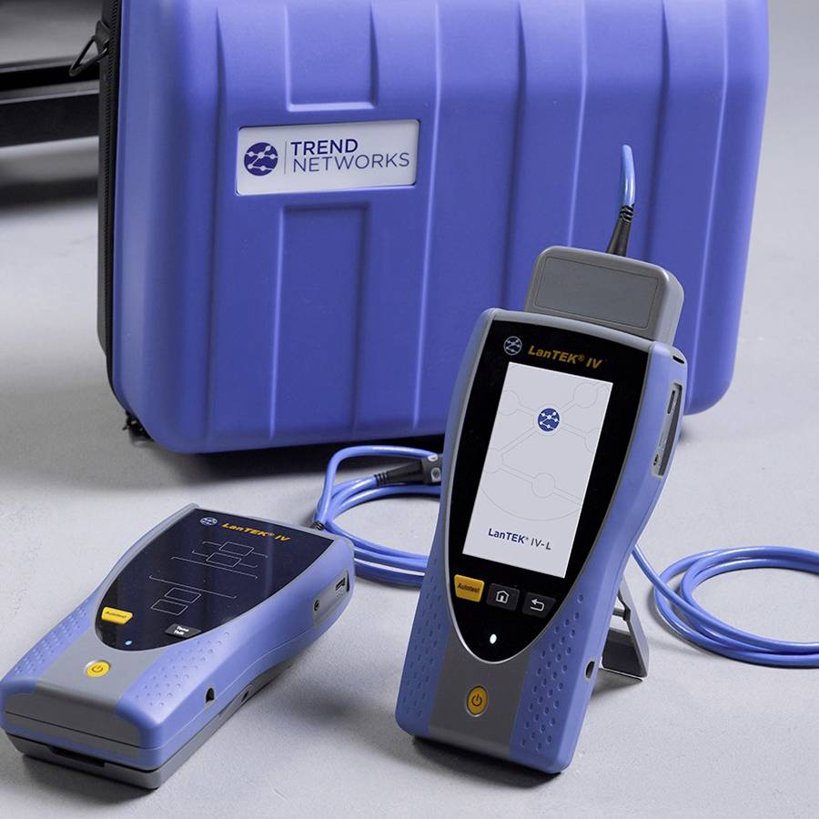 Deux appareils de test réseau avec des écrans et des câbles devant une valise bleue portant l'inscription 'TREND NETWORKS'.