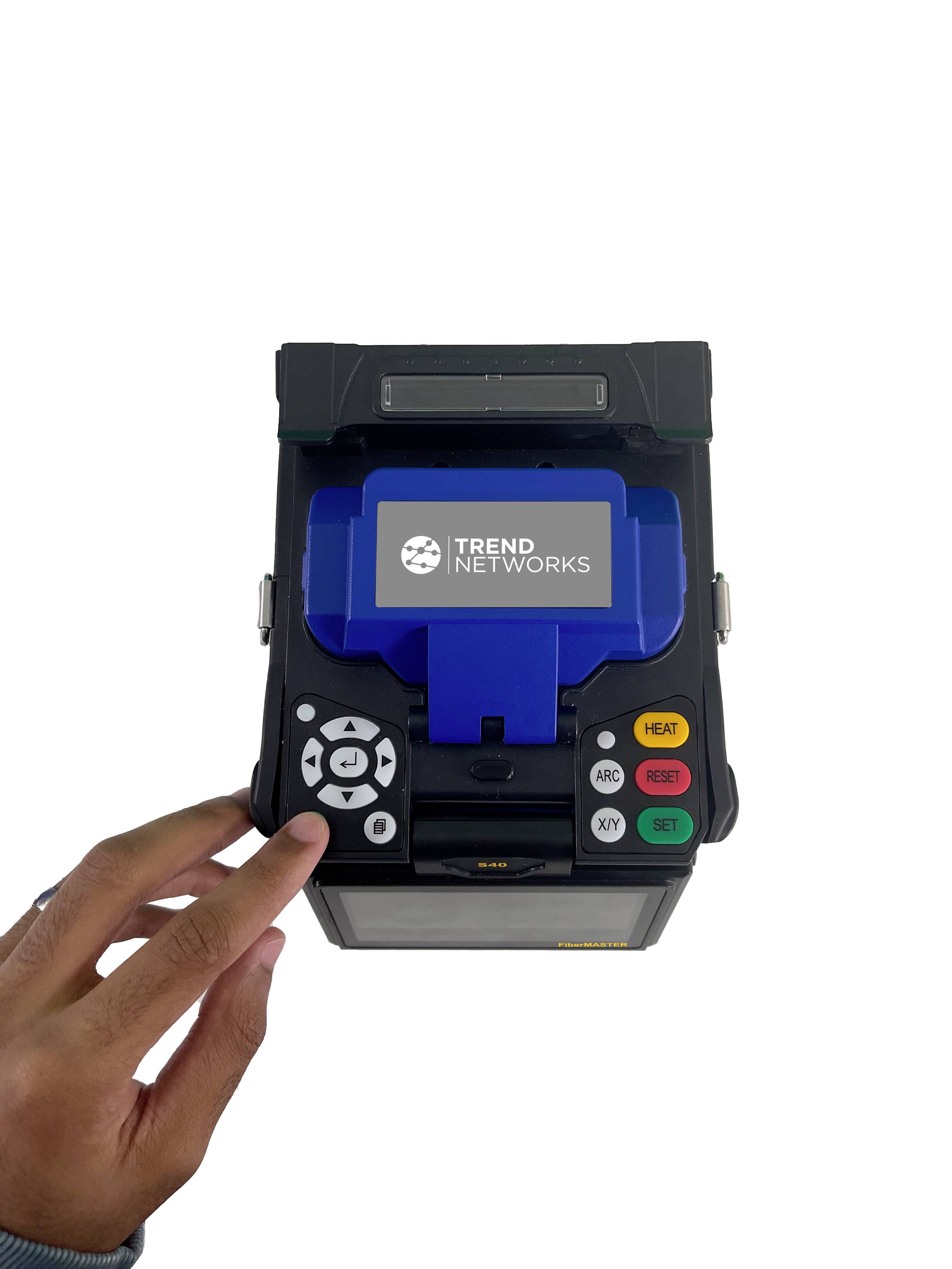 Un appareil avec un écran affichant 'Trend Networks'. Une main actionne les touches.