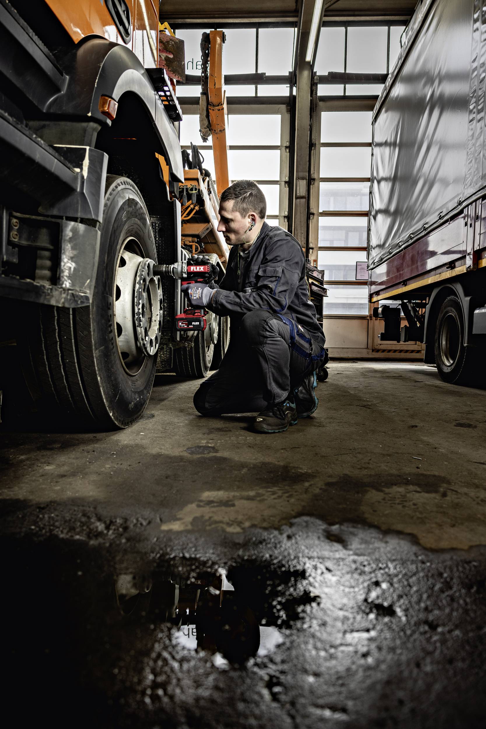 Un mécanicien répare la roue avant d'un camion dans un atelier. D'autres camions sont visibles en arrière-plan.