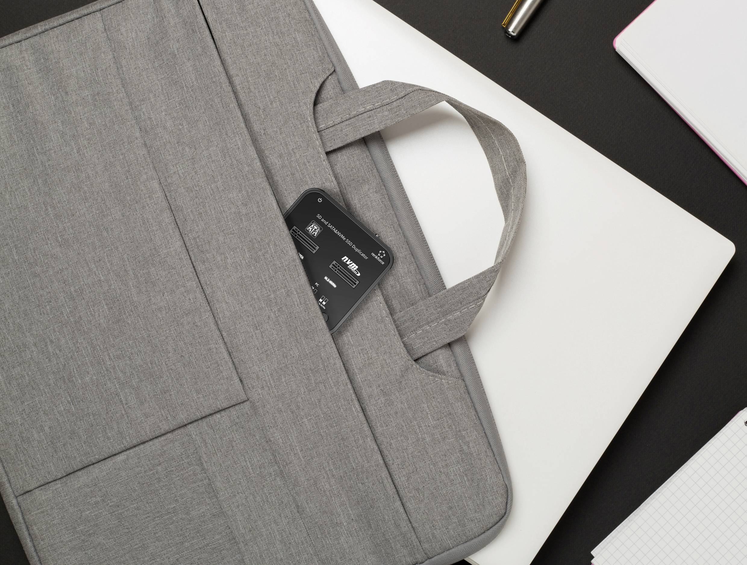 Sacoche grise pour ordinateur portable posée sur une table, à moitié ouverte avec un téléphone portable visible à l'intérieur, entourée d'un ordinateur portable blanc et d'accessoires de bureau.