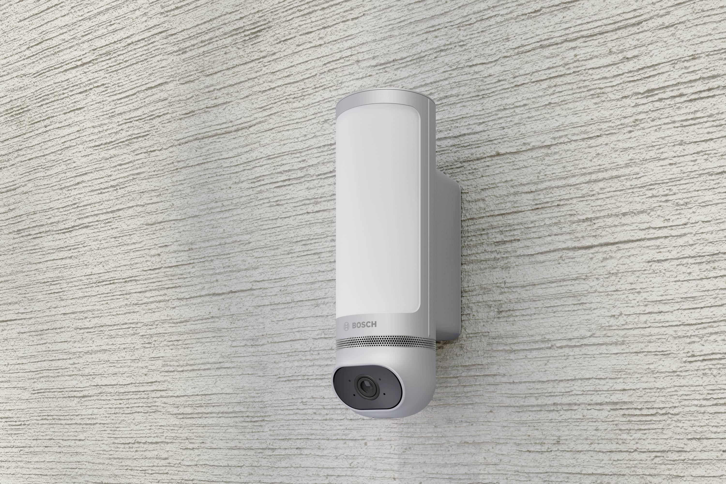 Caméra extérieure avec éclairage intégré, montée sur un mur texturé, offrant sécurité et surveillance de jour comme de nuit.