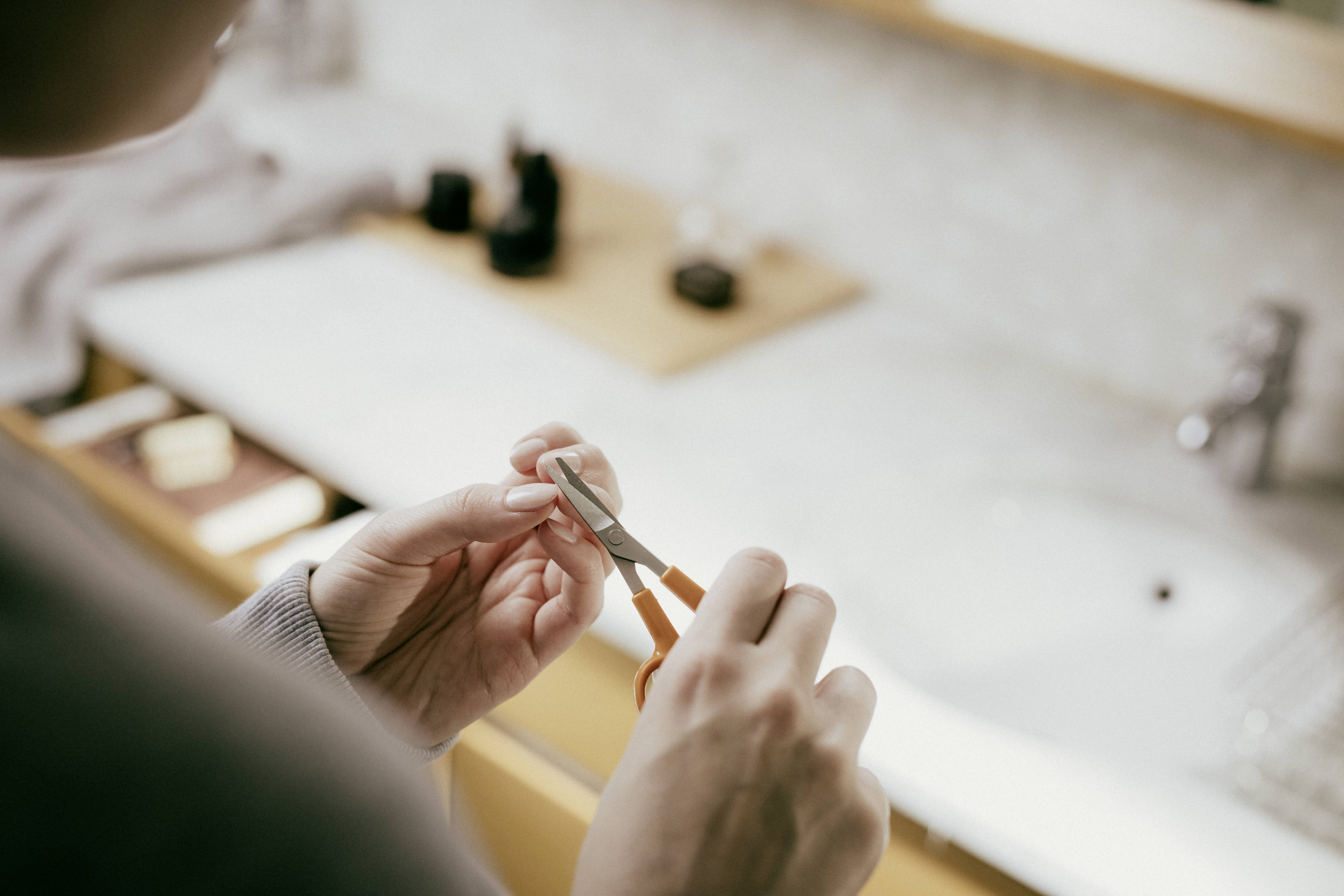 Une personne coupe ses ongles avec des ciseaux à ongles. En arrière-plan, on peut voir une salle de bain avec un lavabo.