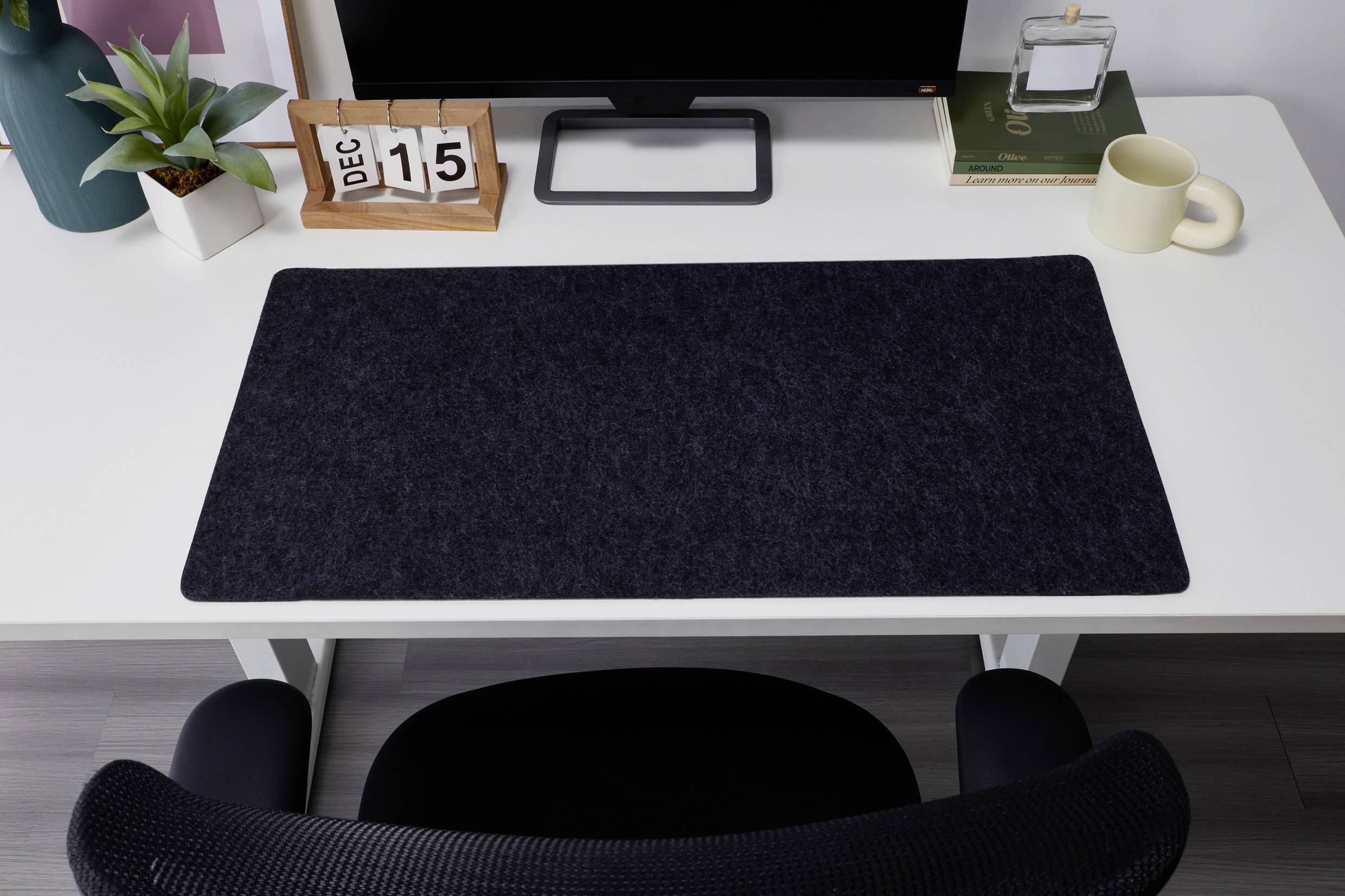 Bureau avec un sous-main noir, le calendrier affiche '15 déc', un moniteur, une plante, un livre, une tasse et des lunettes à côté.