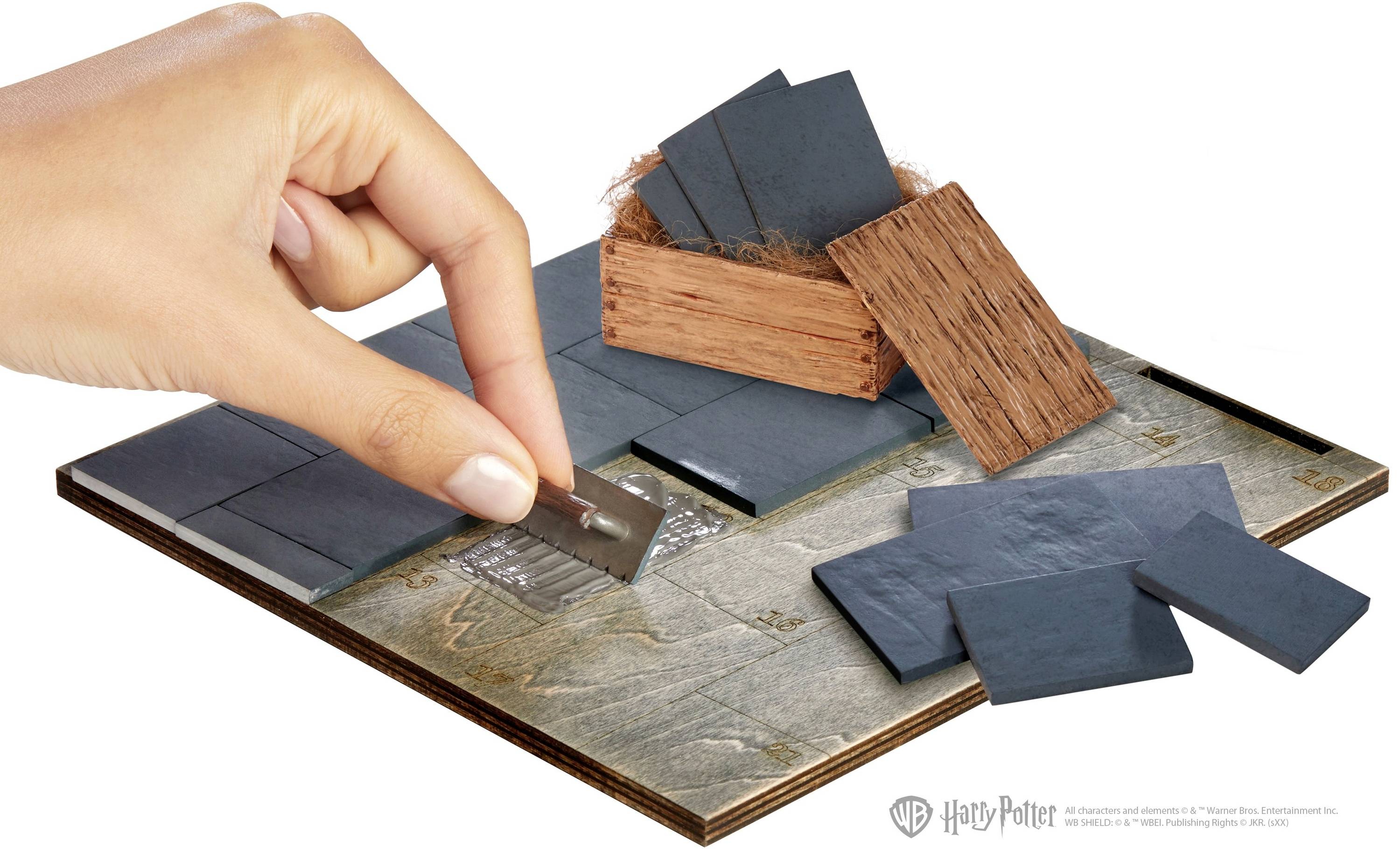 Une main tient une lame de rasoir et découpe un objet rectangulaire, noir et fin à partir d'une tuile sur une planche en bois.