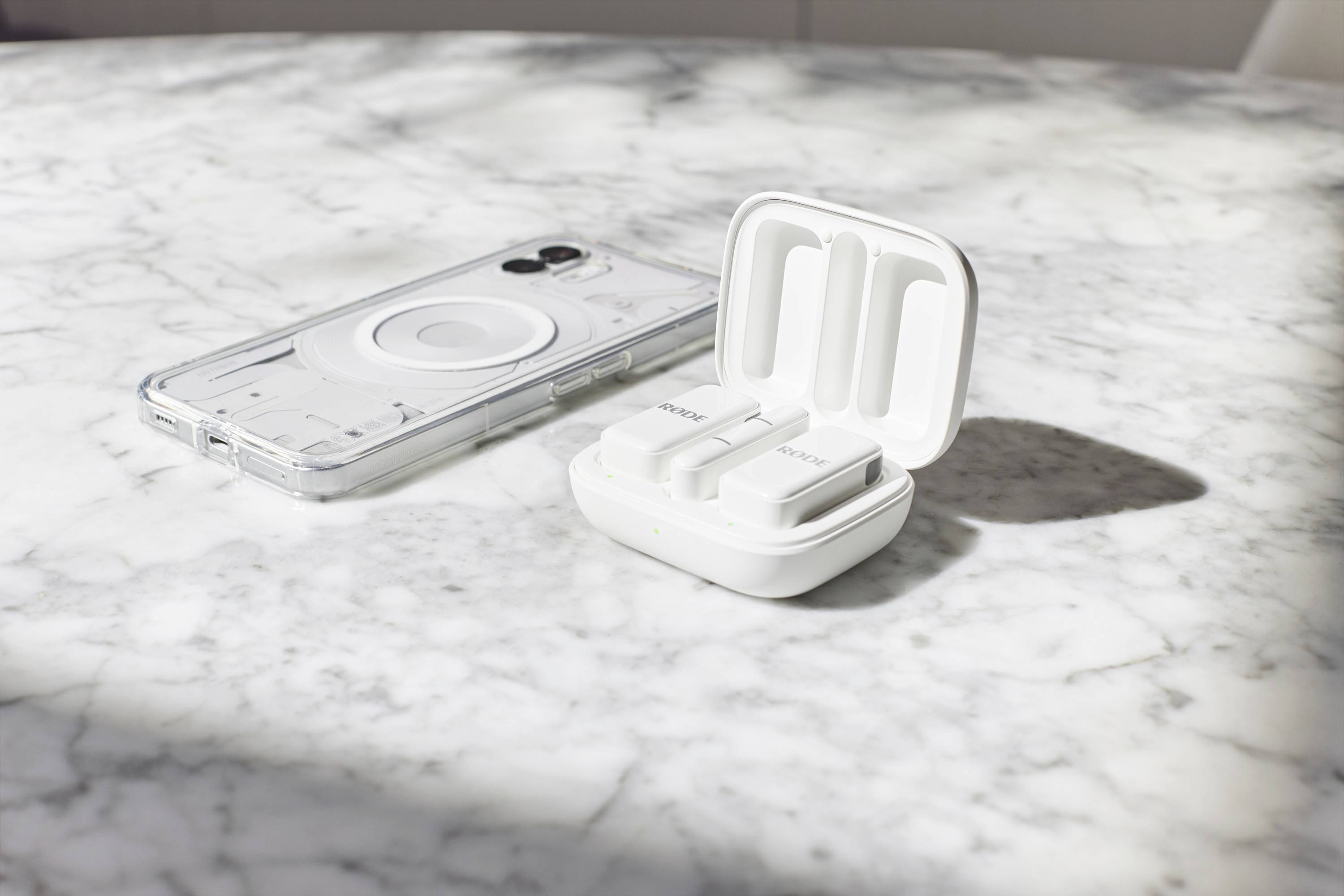 Un étui de téléphone transparent est posé sur une table en marbre à côté d'un boîtier de chargement blanc ouvert contenant deux écouteurs sans fil.