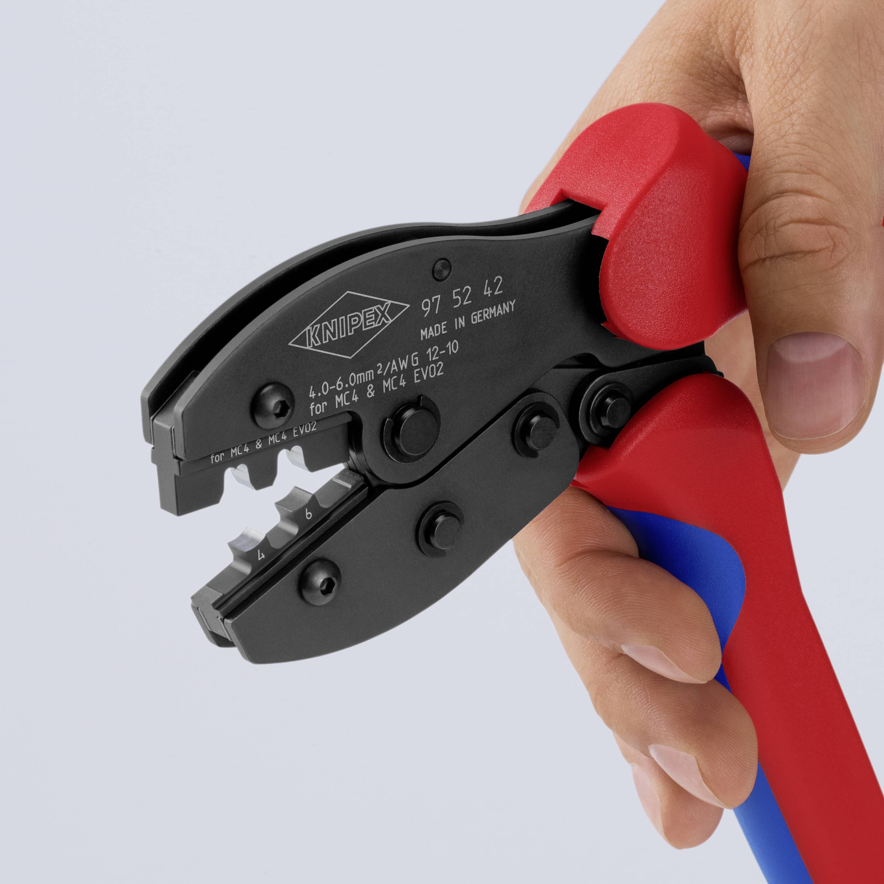 Un outil de sertissage avec une poignée rouge et bleue est tenu par une main, adapté aux contacts électriques isolés.