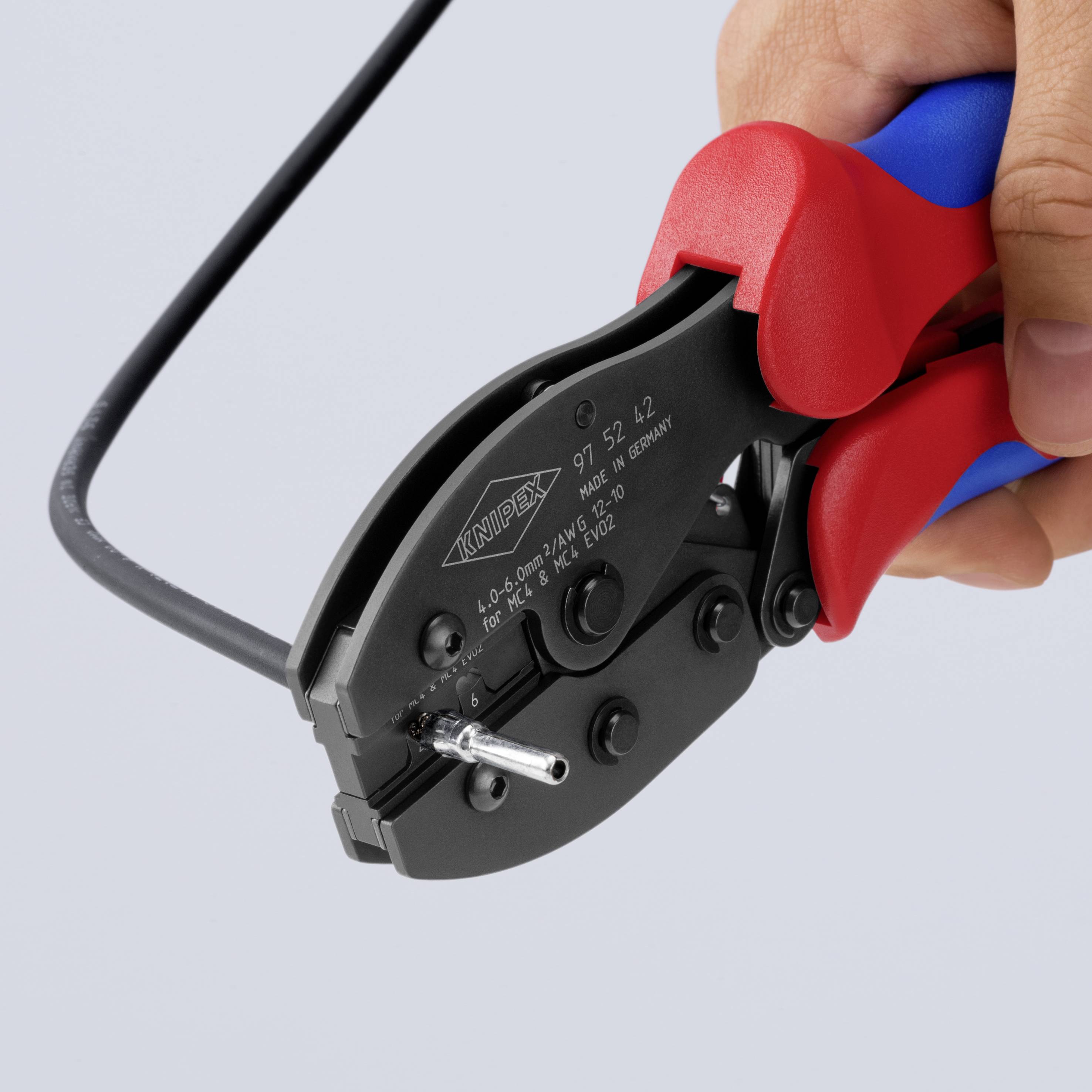 Gros plan d'un outil à sertir rouge et bleu tenu dans une main, en train de traiter un câble électrique noir.