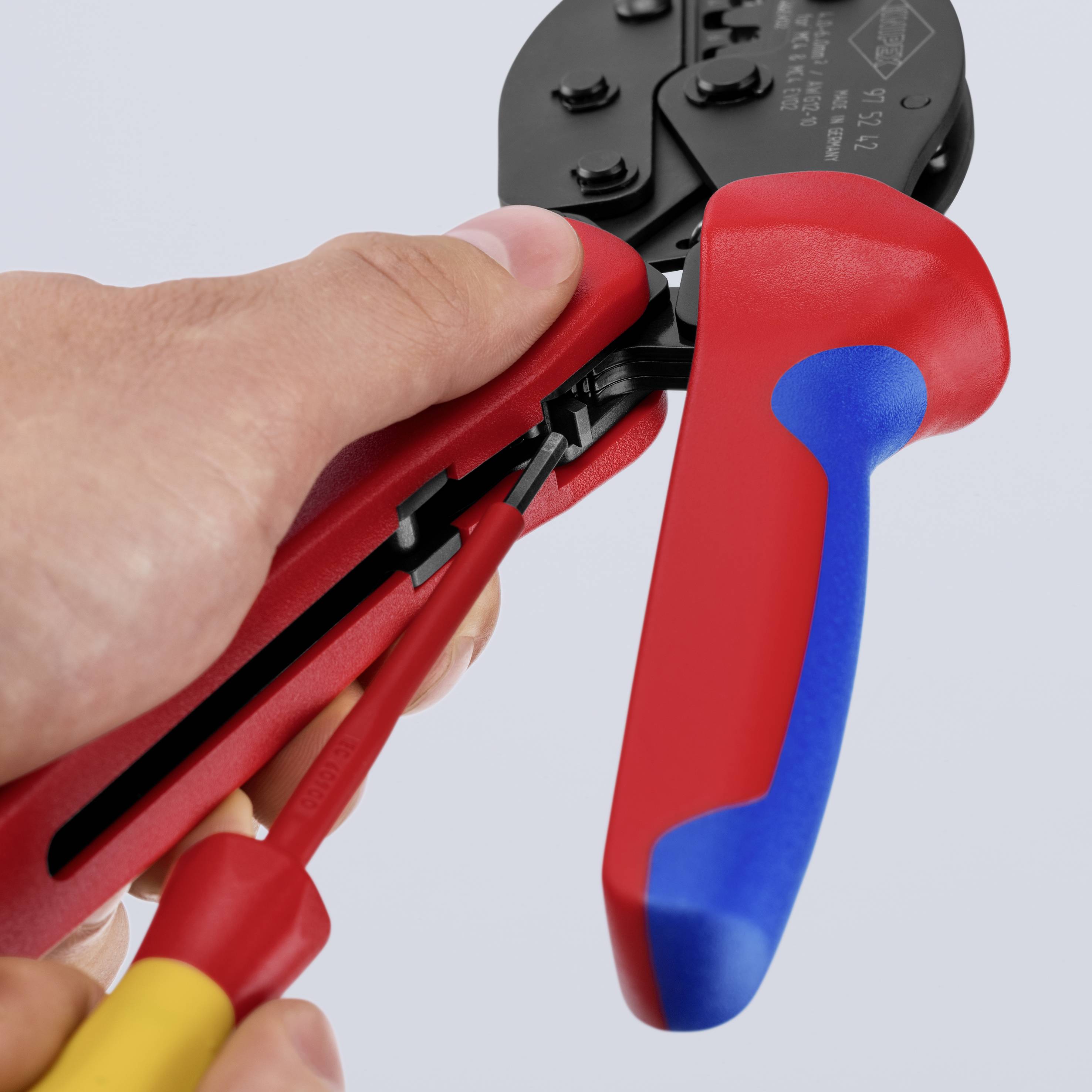 Une main tient une pince à sertir rouge et connecte un câble à un connecteur, mettant l'accent sur la précision et la manipulation.