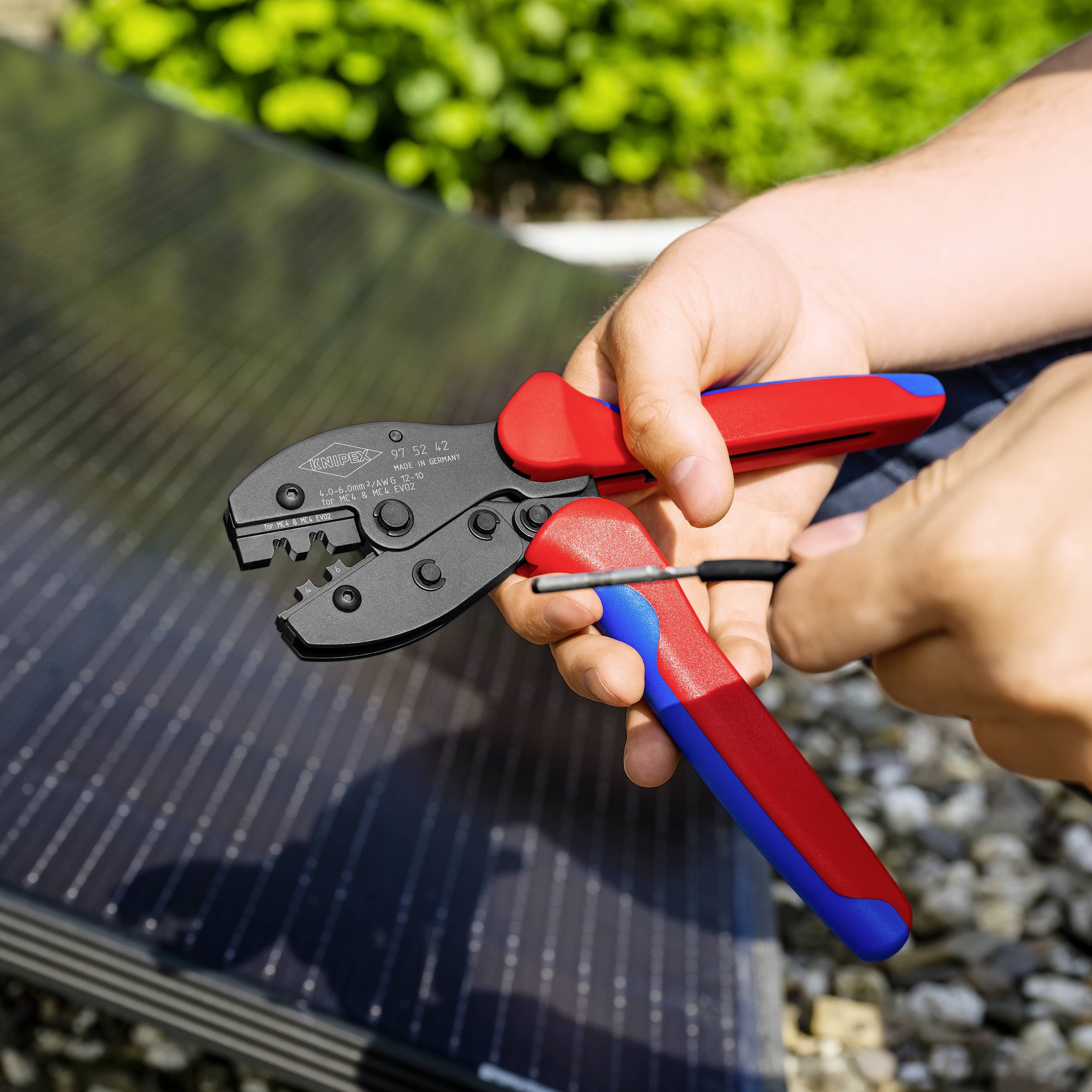 Une personne tient un outil de sertissage et travaille sur un panneau solaire. La scène montre une activité artisanale en extérieur.