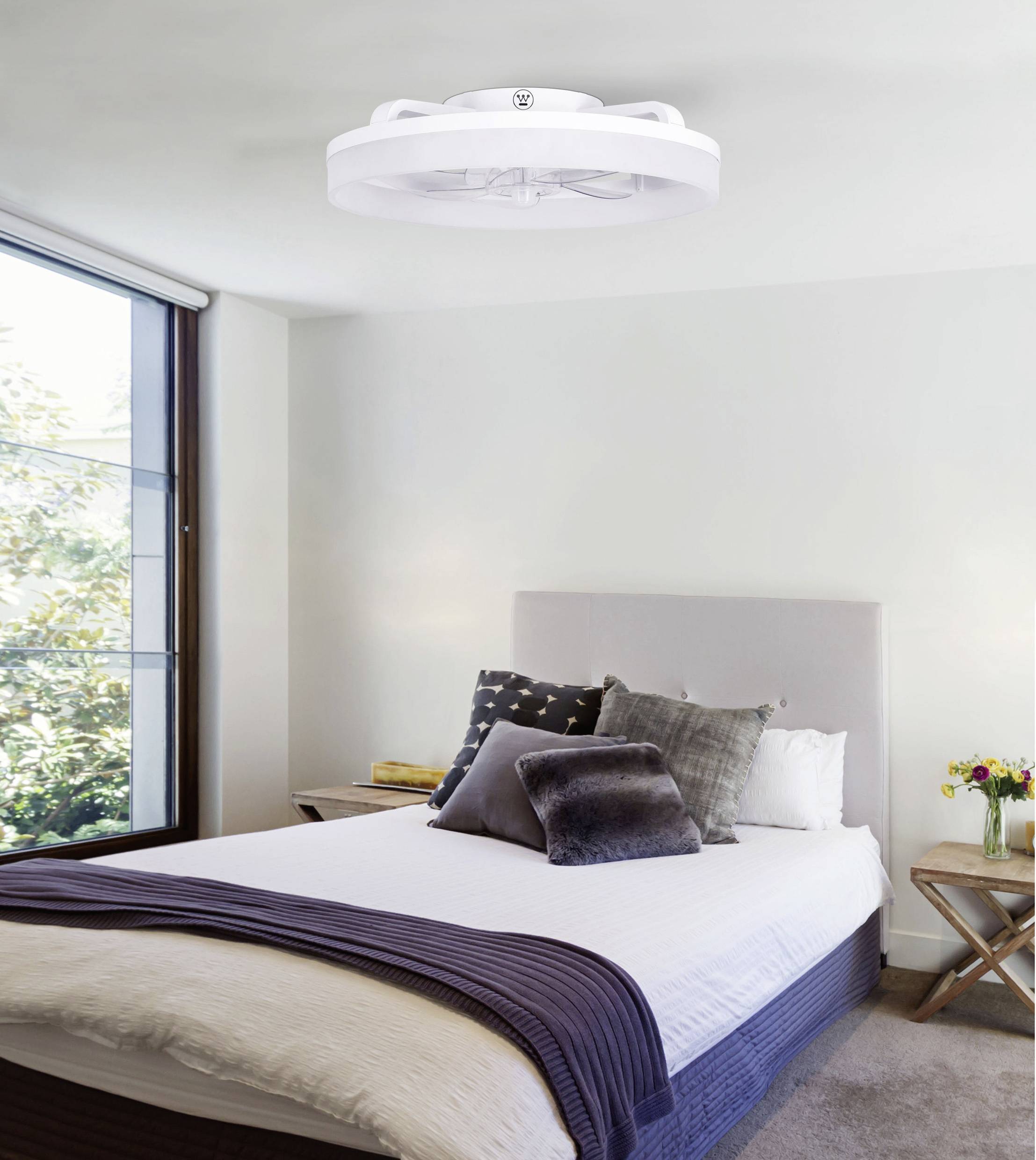 Chambre à coucher avec un grand lit, des oreillers et des couvertures. Au plafond, une lampe moderne et ronde. La fenêtre offre une vue sur les arbres.