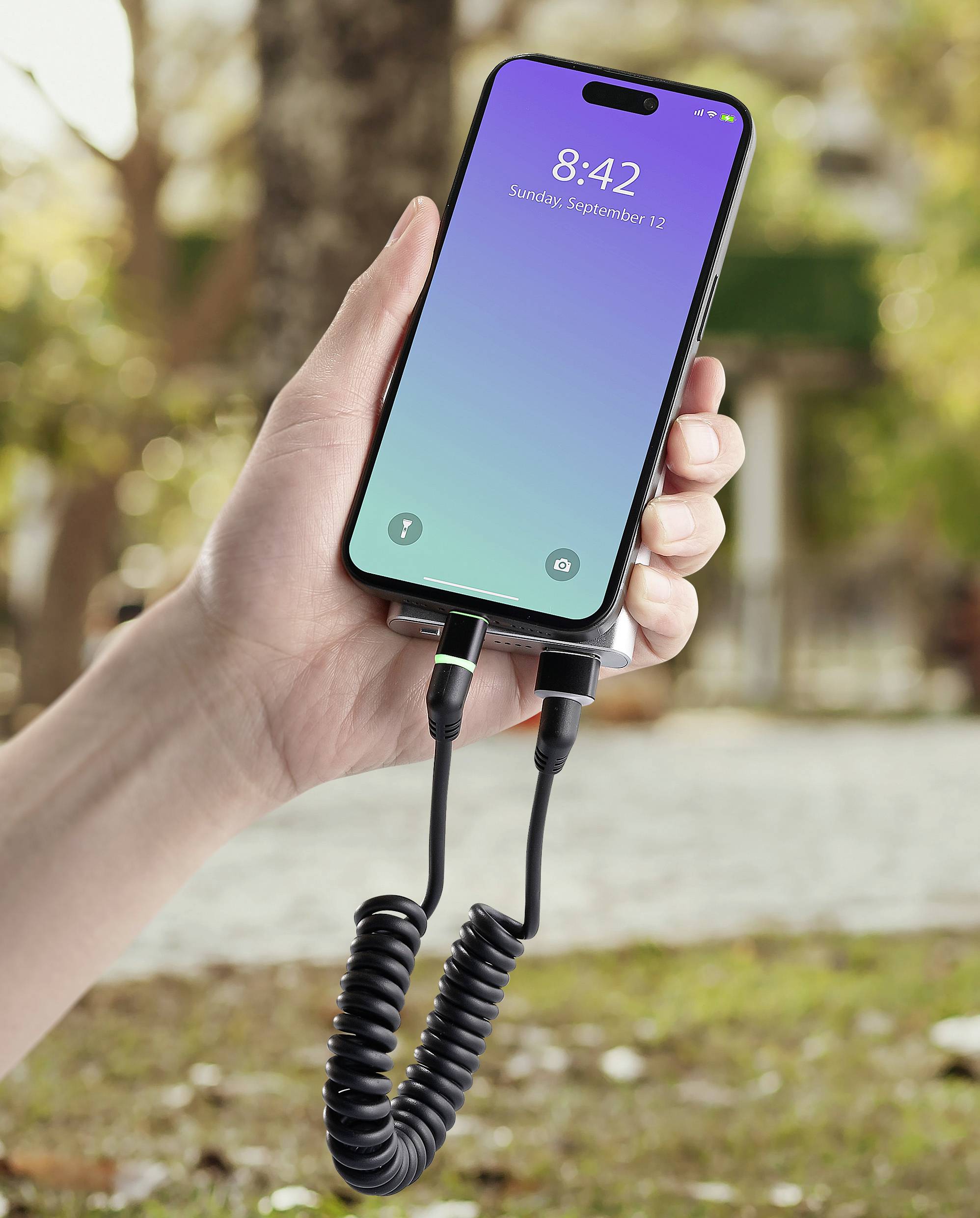 Une main tient un smartphone à l'écran verrouillé, sur lequel on peut lire '8:42 ; dimanche 12 septembre'. L'appareil est connecté par un câble spiralé.