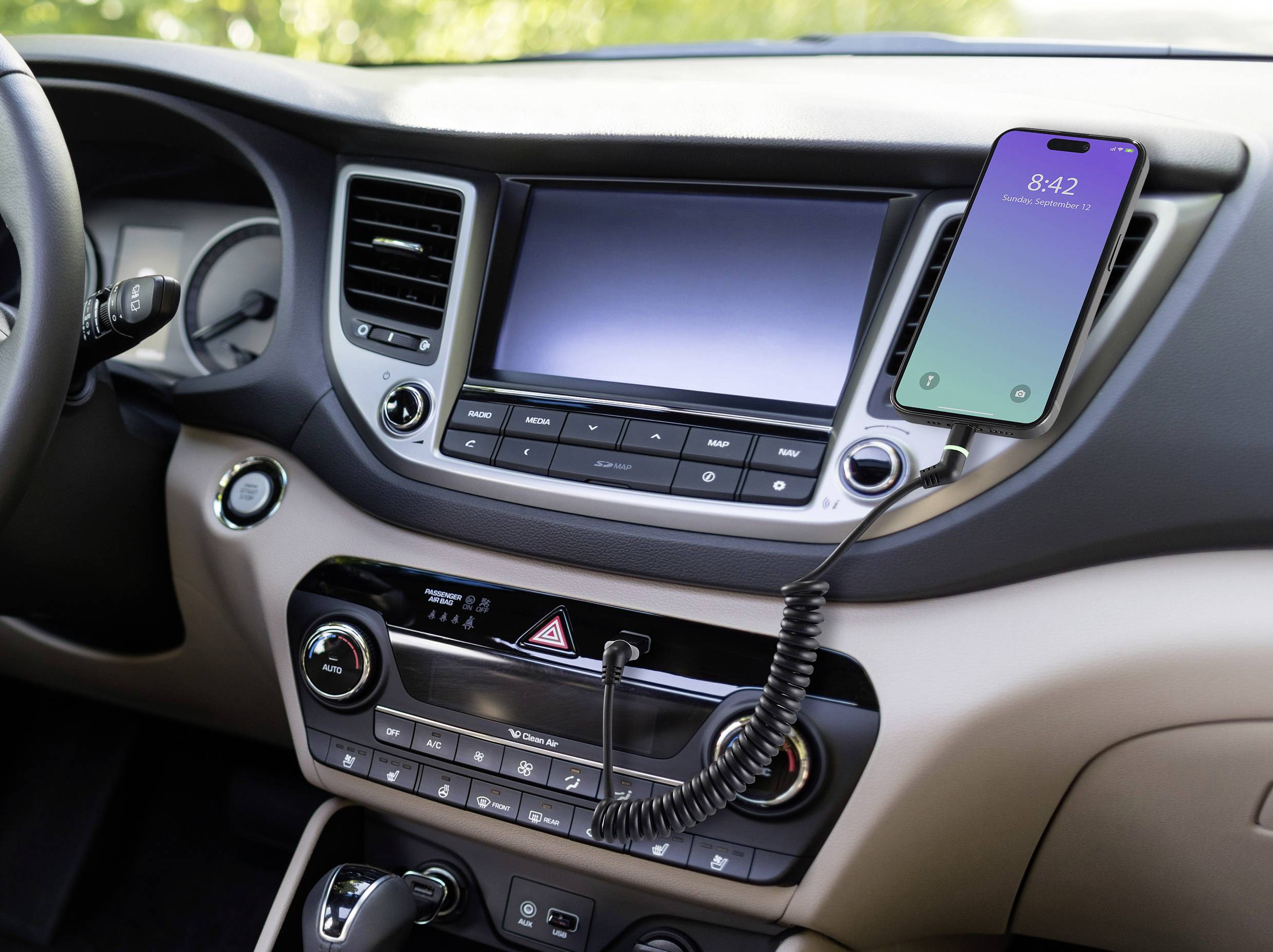 Un smartphone est connecté au tableau de bord de l'intérieur d'une voiture avec un câble. L'écran affiche '8:42'.