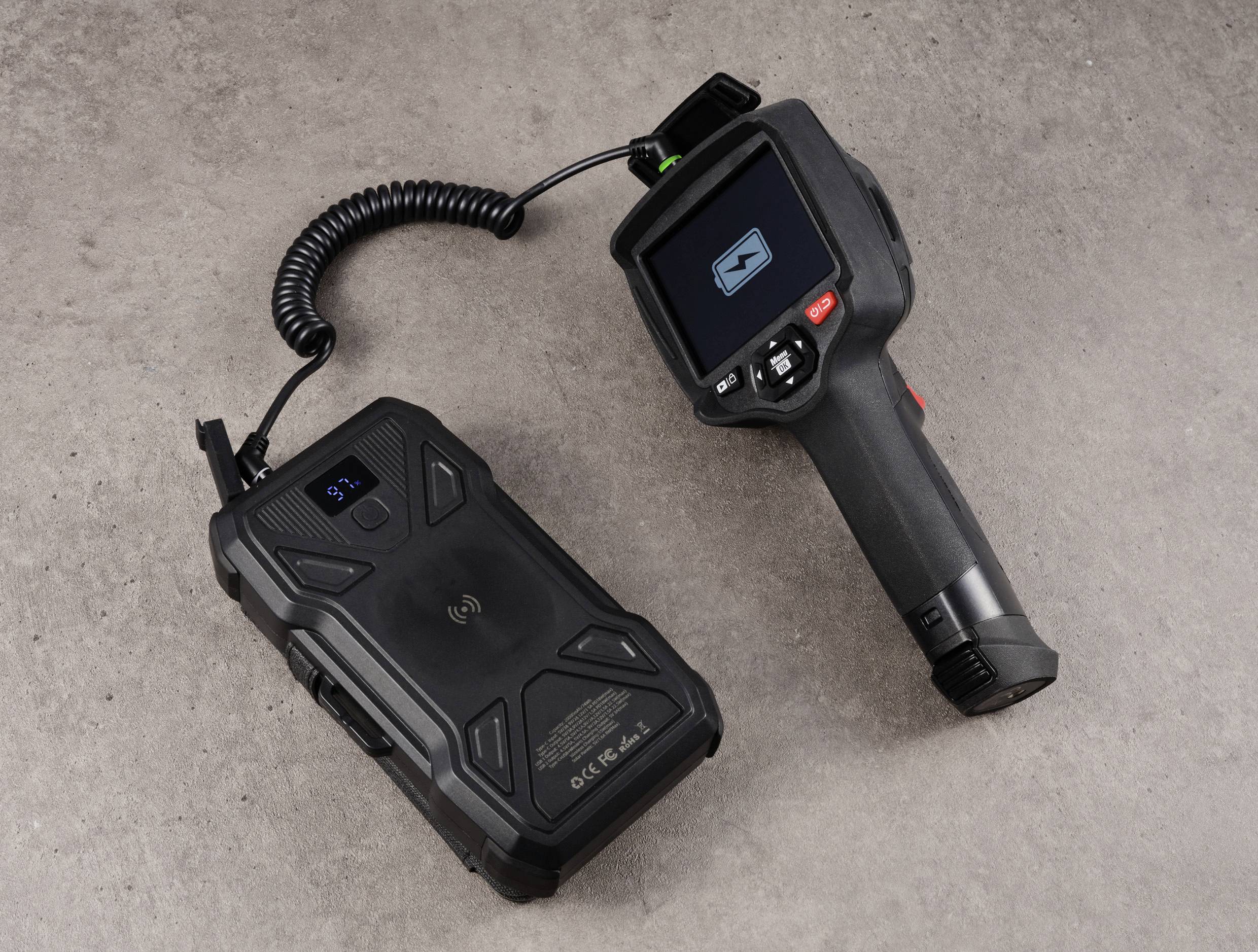 Scanner portable d'inspection avec écran et unité portable, reliés par un câble, sur une surface grise texturée.