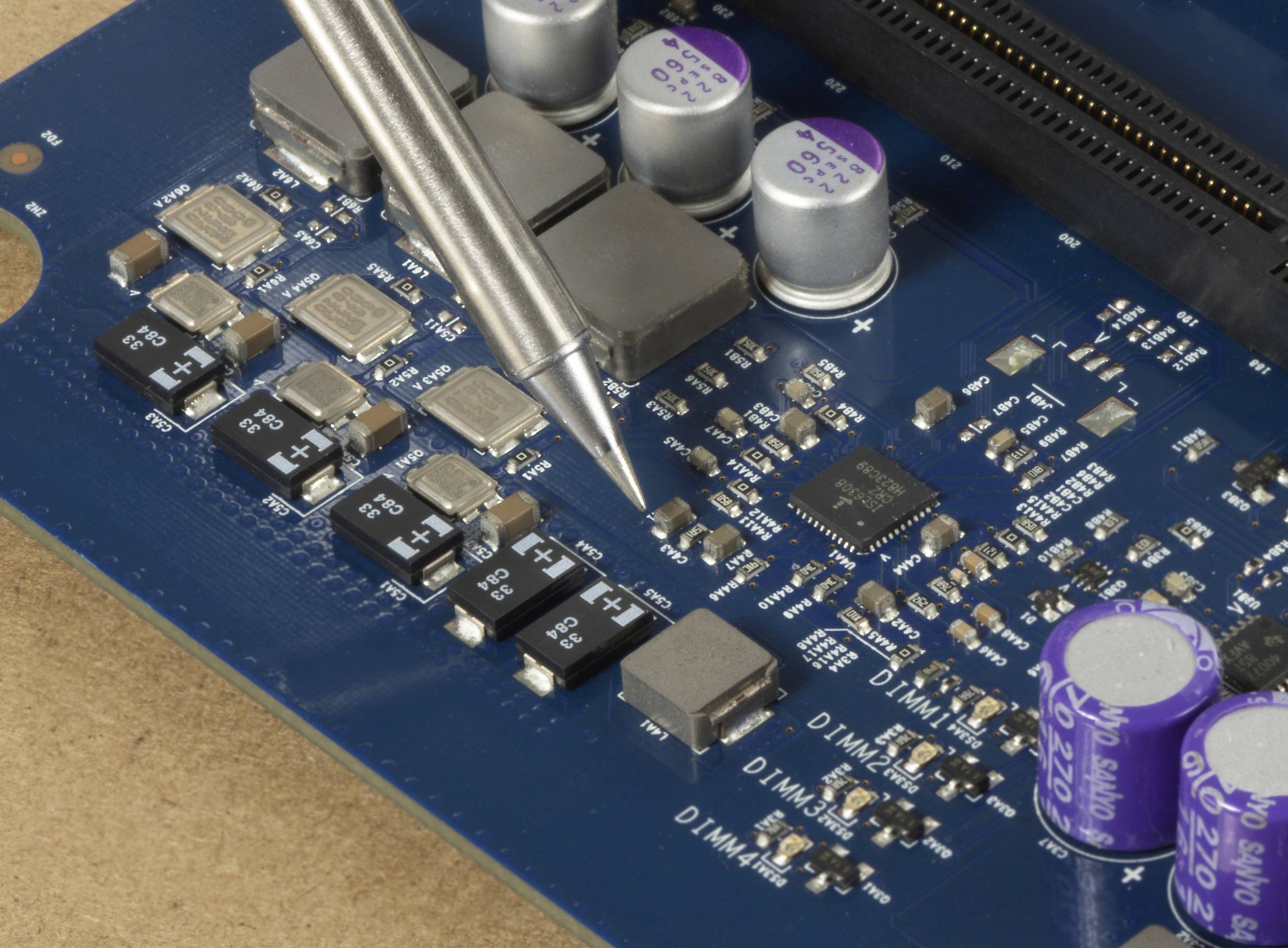 Gros plan d'un circuit imprimé bleu avec une puce électronique et des composants électroniques. Un fer à souder touche la carte.
