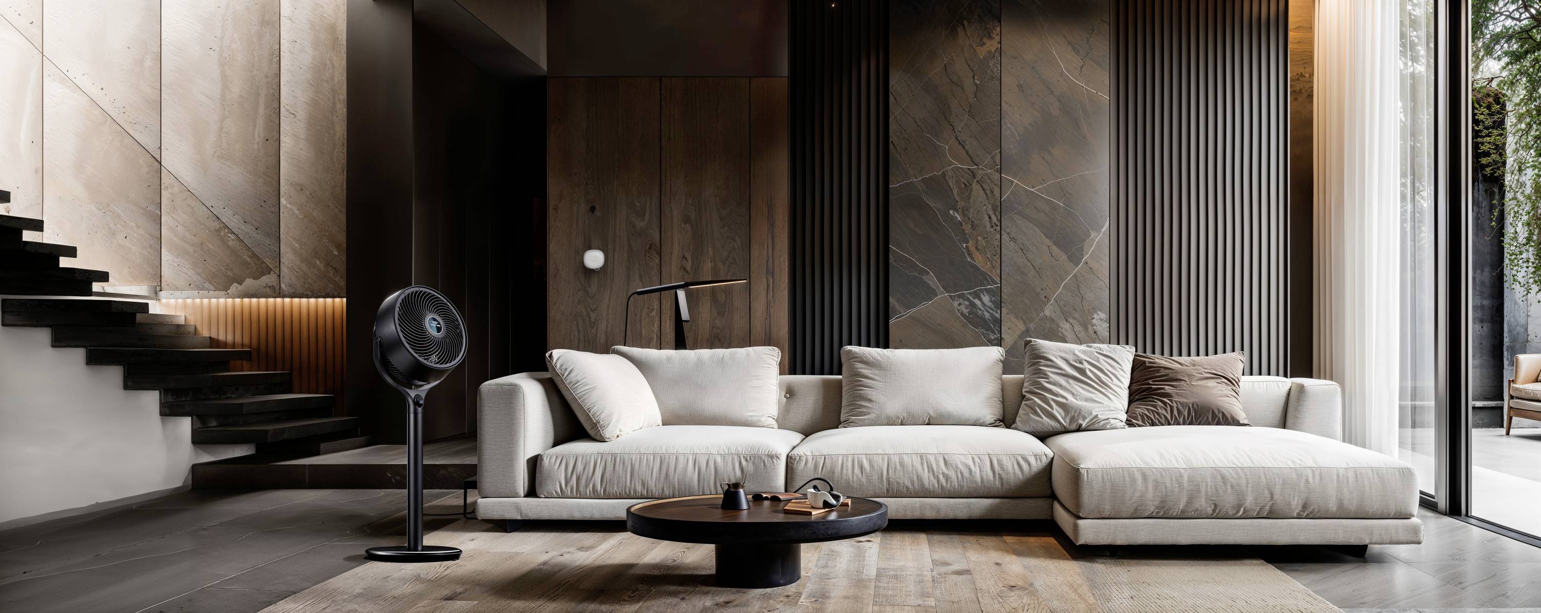 Salon moderne avec un canapé beige, une table basse ronde et un lampadaire. Murs en bois et escalier sur la gauche, grandes fenêtres à droite.