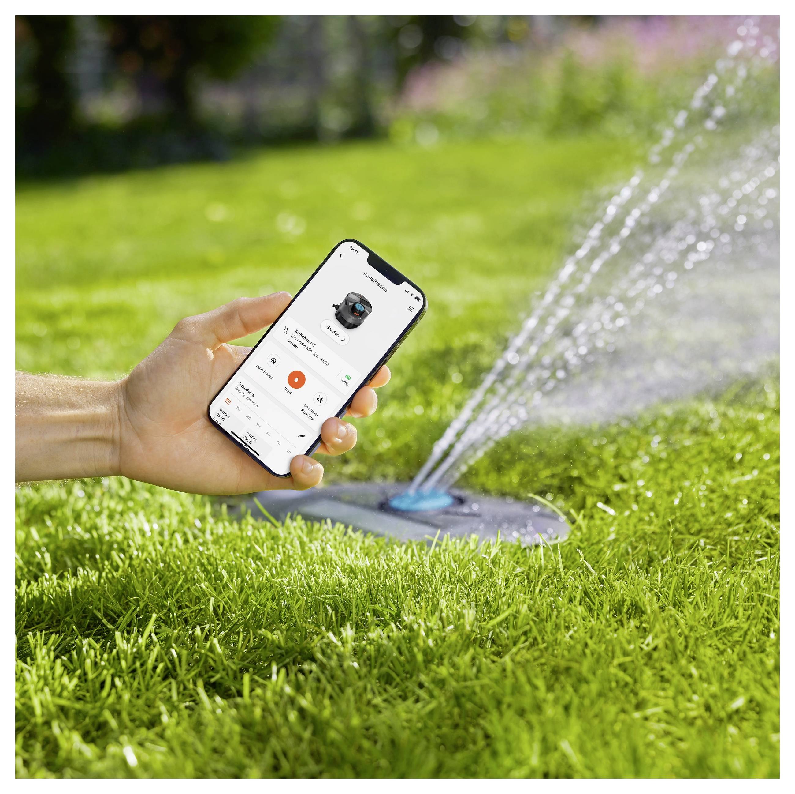 Une main tenant un smartphone avec une application d'irrigation contrôle un arroseur qui arrose une pelouse verte, mettant en avant la technologie de la maison intelligente.