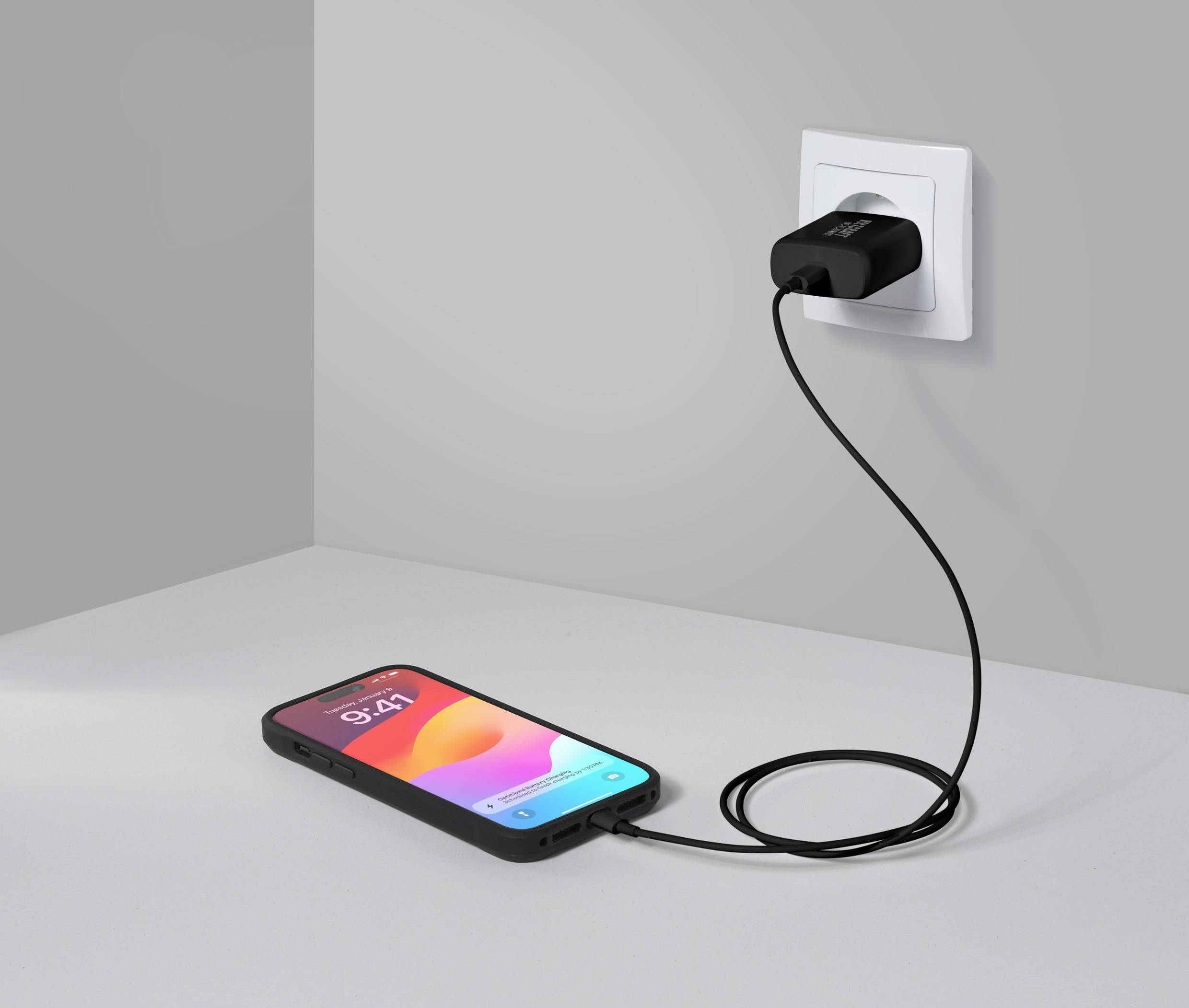 Un smartphone est posé sur une table et se charge via un câble branché à un chargeur connecté à une prise murale.