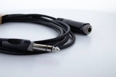 Un câble audio noir avec une fiche jack 6,35 mm et une prise est posé sur un fond blanc.