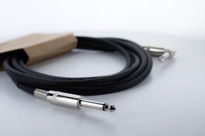 Un câble audio noir avec des fiches métalliques est posé sur une surface blanche.