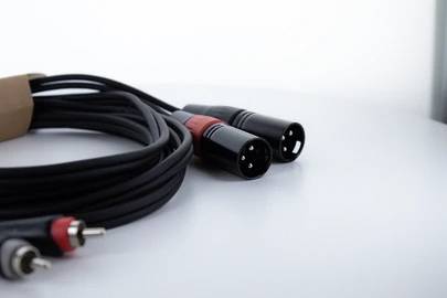 Une paire de câbles XLR avec des fiches noires et des marquages rouges est posée sur une table blanche. Le câble est partiellement enroulé.