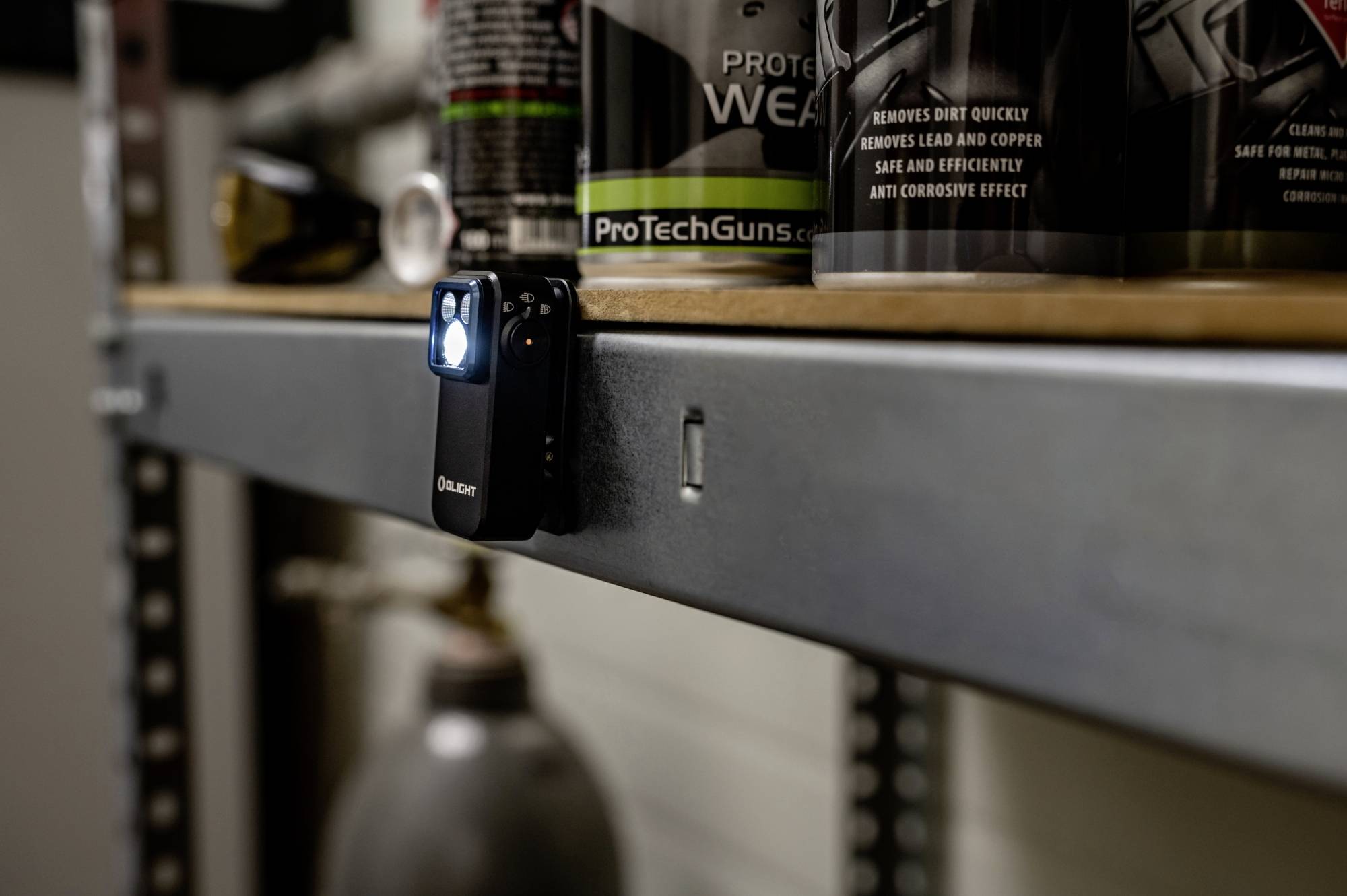 Petite lampe de poche allumée, fixée à une étagère métallique dans un atelier. Des produits d'entretien pour armes sont visibles en arrière-plan.
