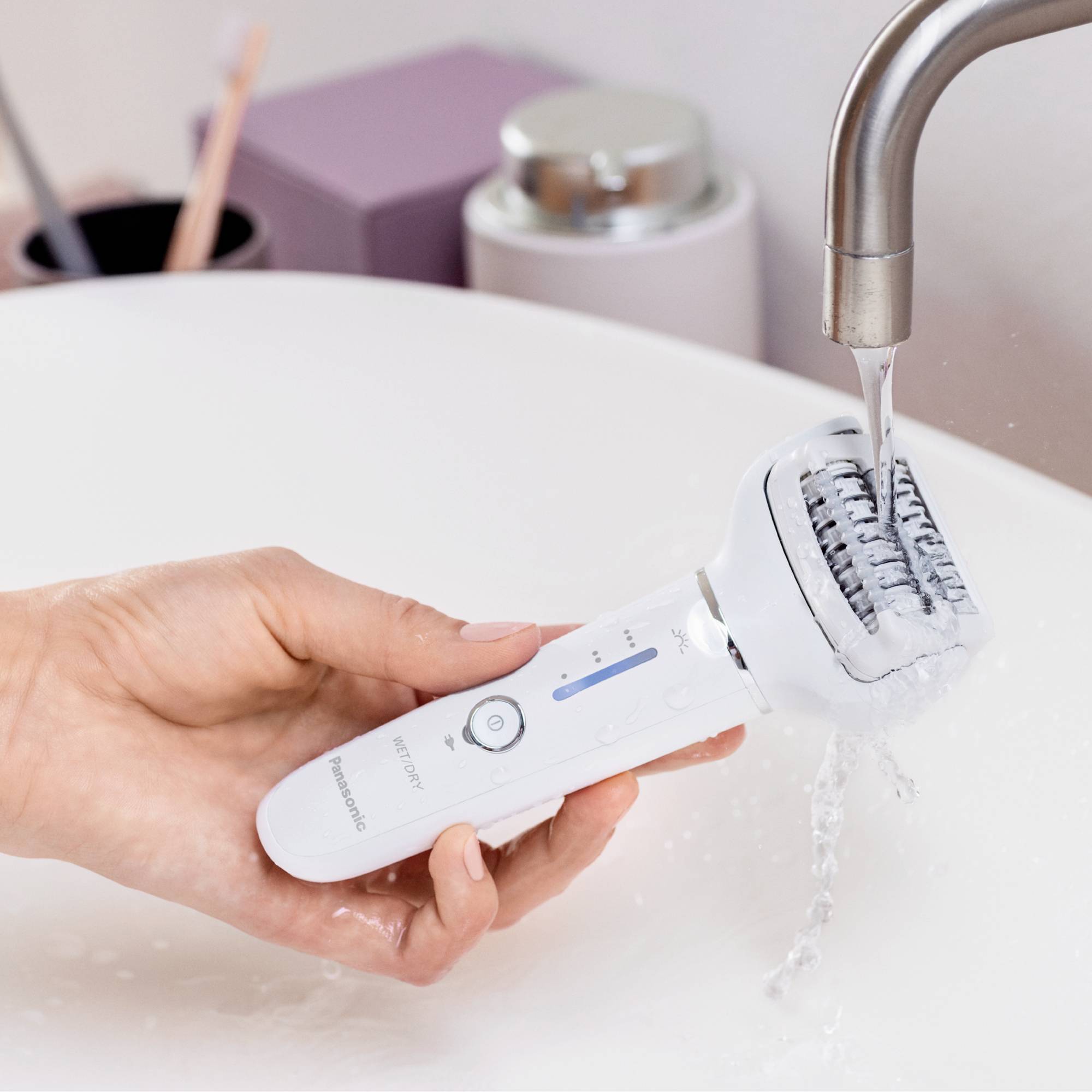 Une main tient un épilateur électrique sous l'eau courante dans un lavabo pour le nettoyer.