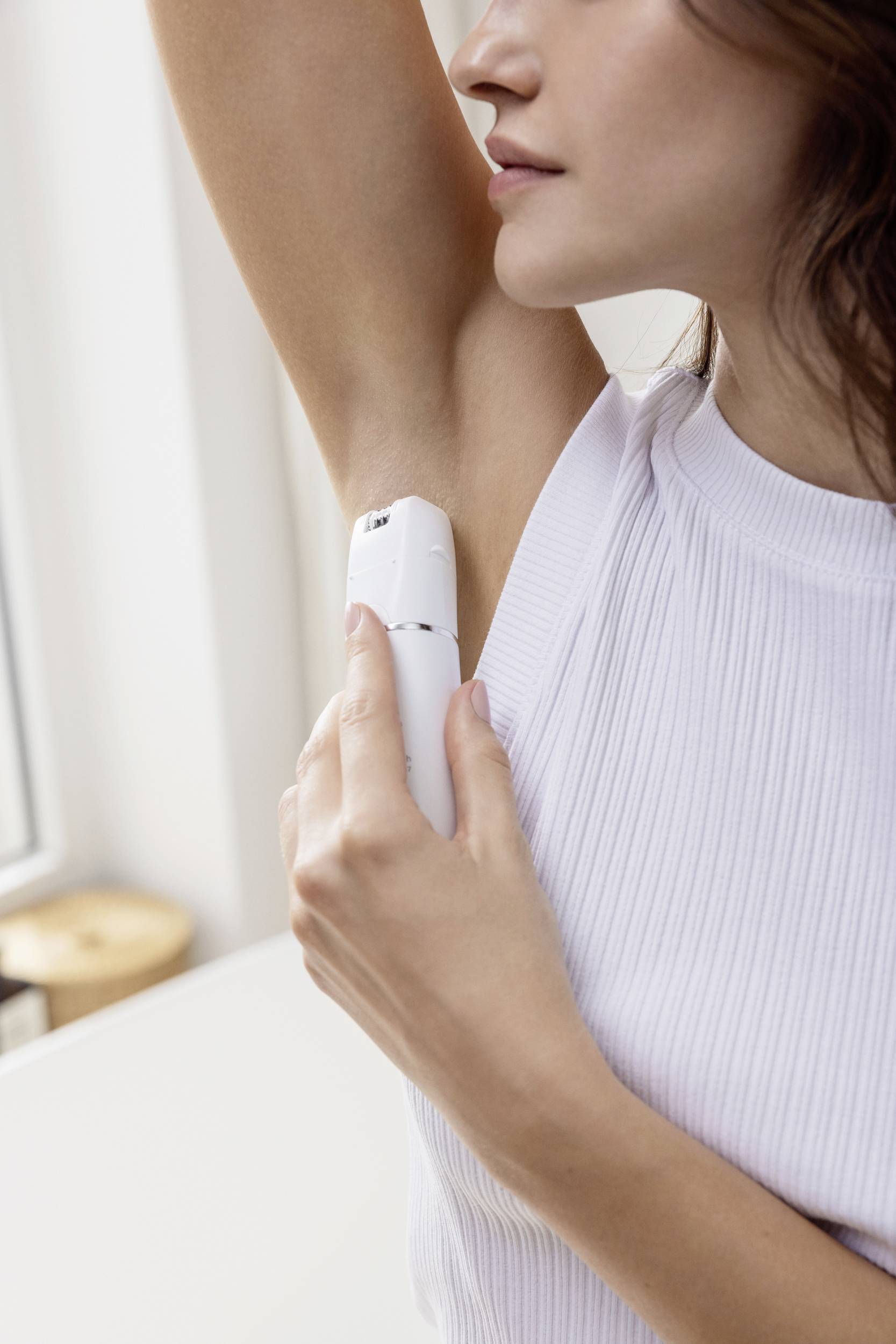 Une femme portant un haut blanc applique du déodorant sous son bras gauche.